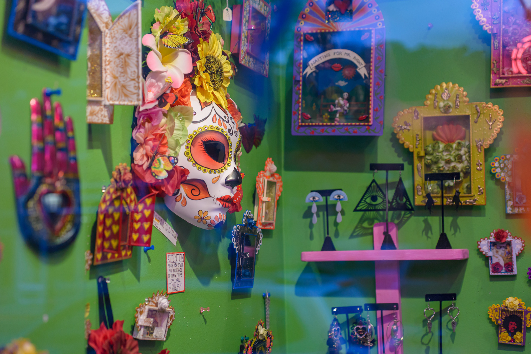 Shop display of various spiritually oriented objects including a feminine folk mask on the left which is the main focus of the image.