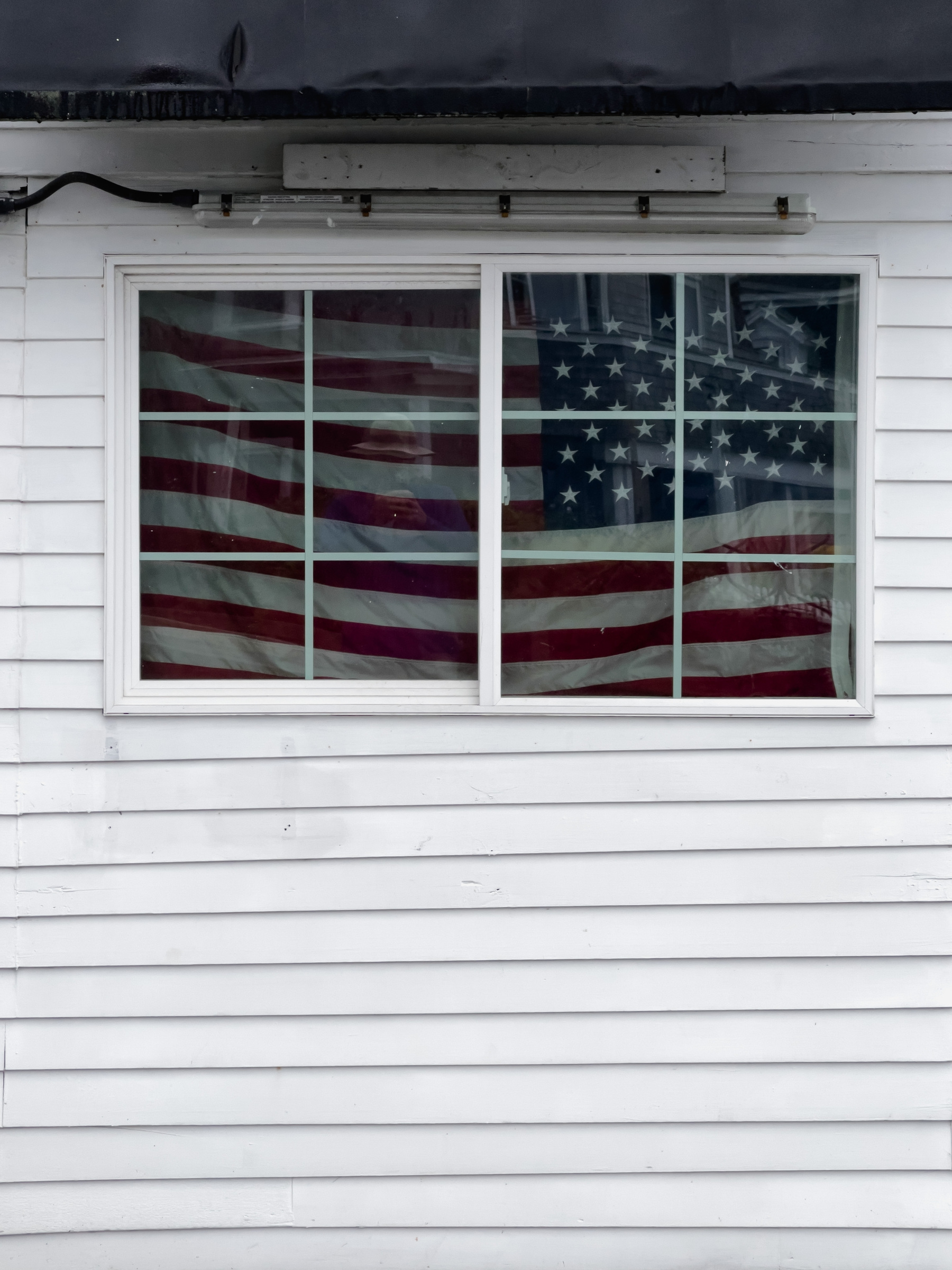 American flag in window in clapboard wall of building.