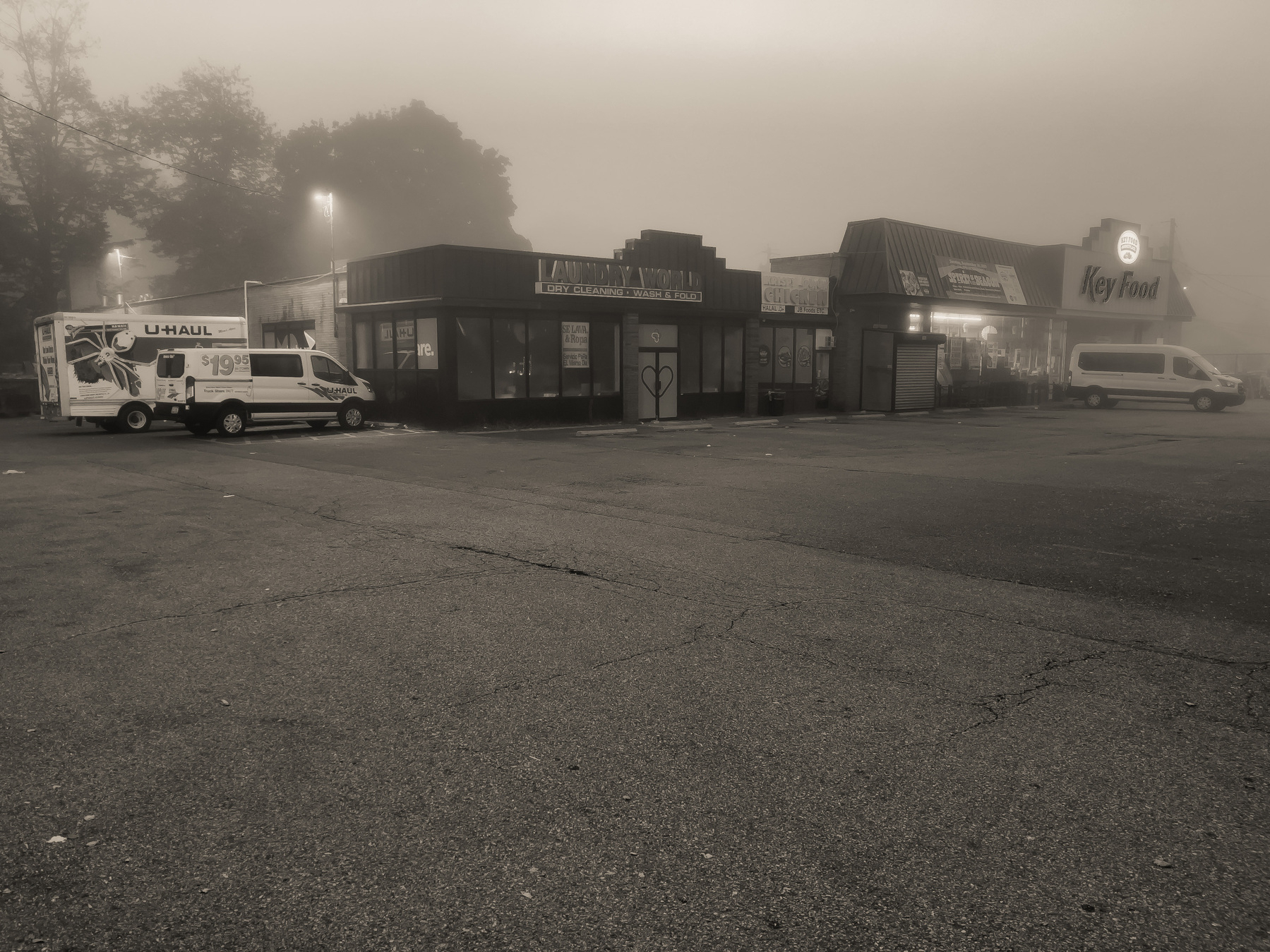Small shopping mall across a parking lot shrouded in fog.