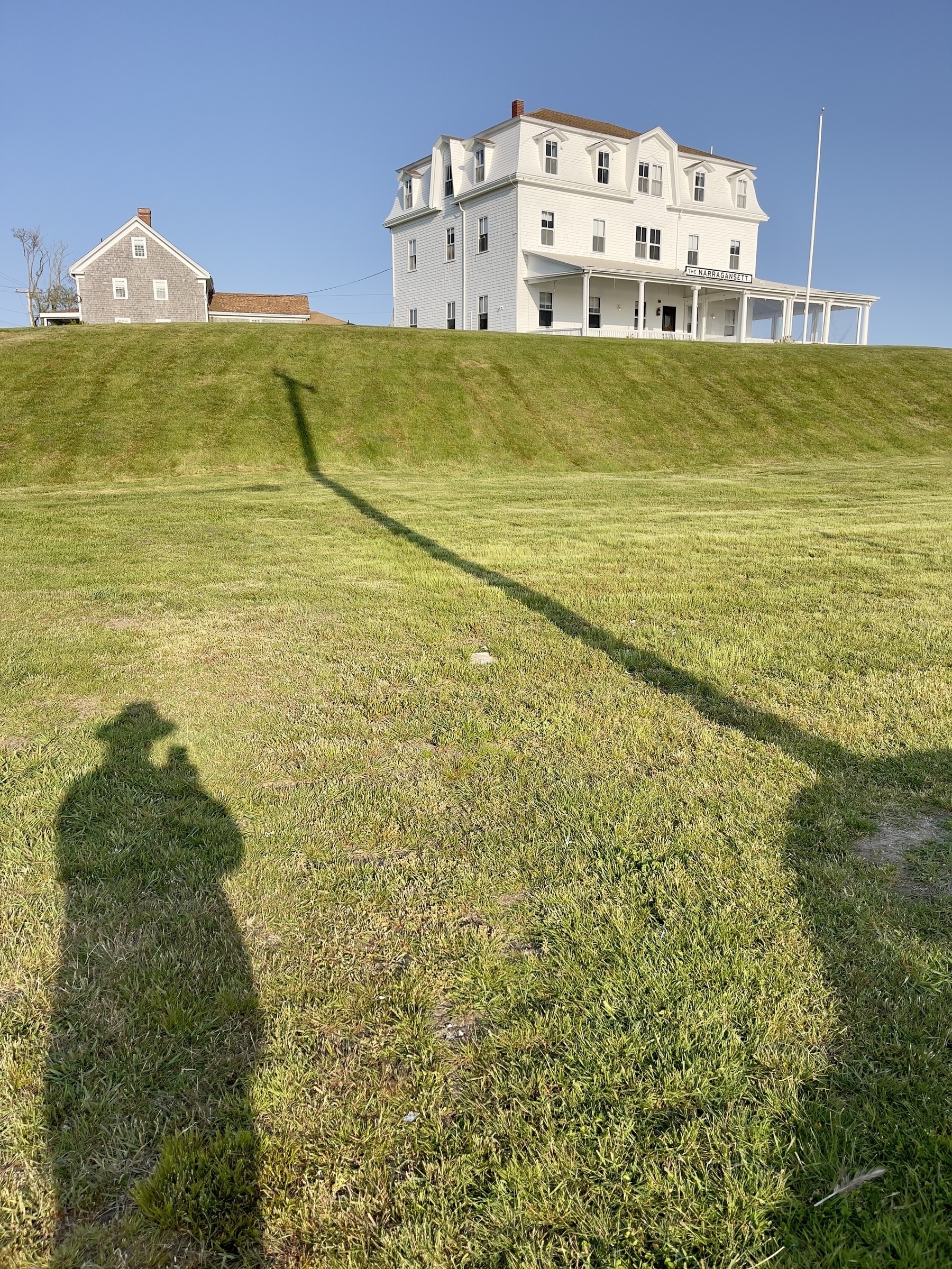Narragansett Inn on hill with my shadow and shadow of utility pole in the foreground.
