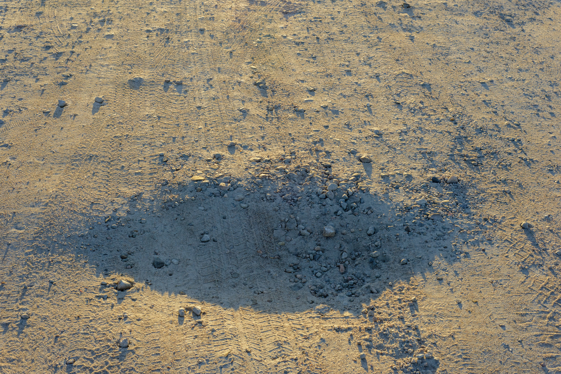 Crater in a parking lot with low angle sun casting a shadow across most of the bowl of the crater.