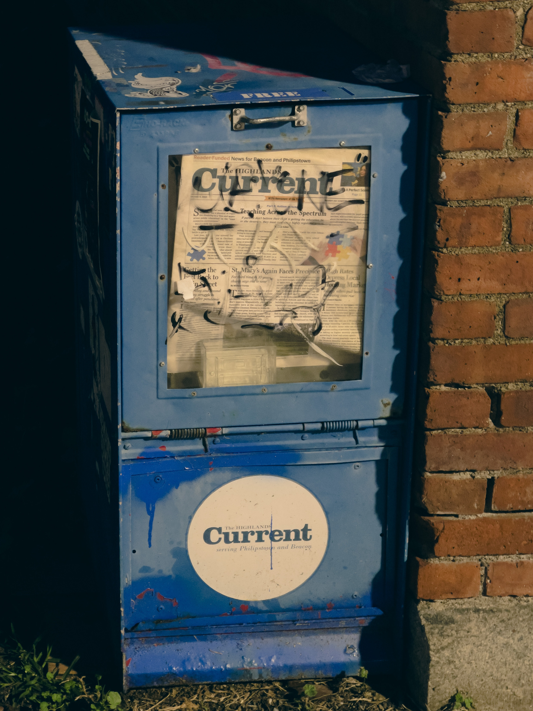 Blue newspaper dispenser box with Highland Current logo and papers.