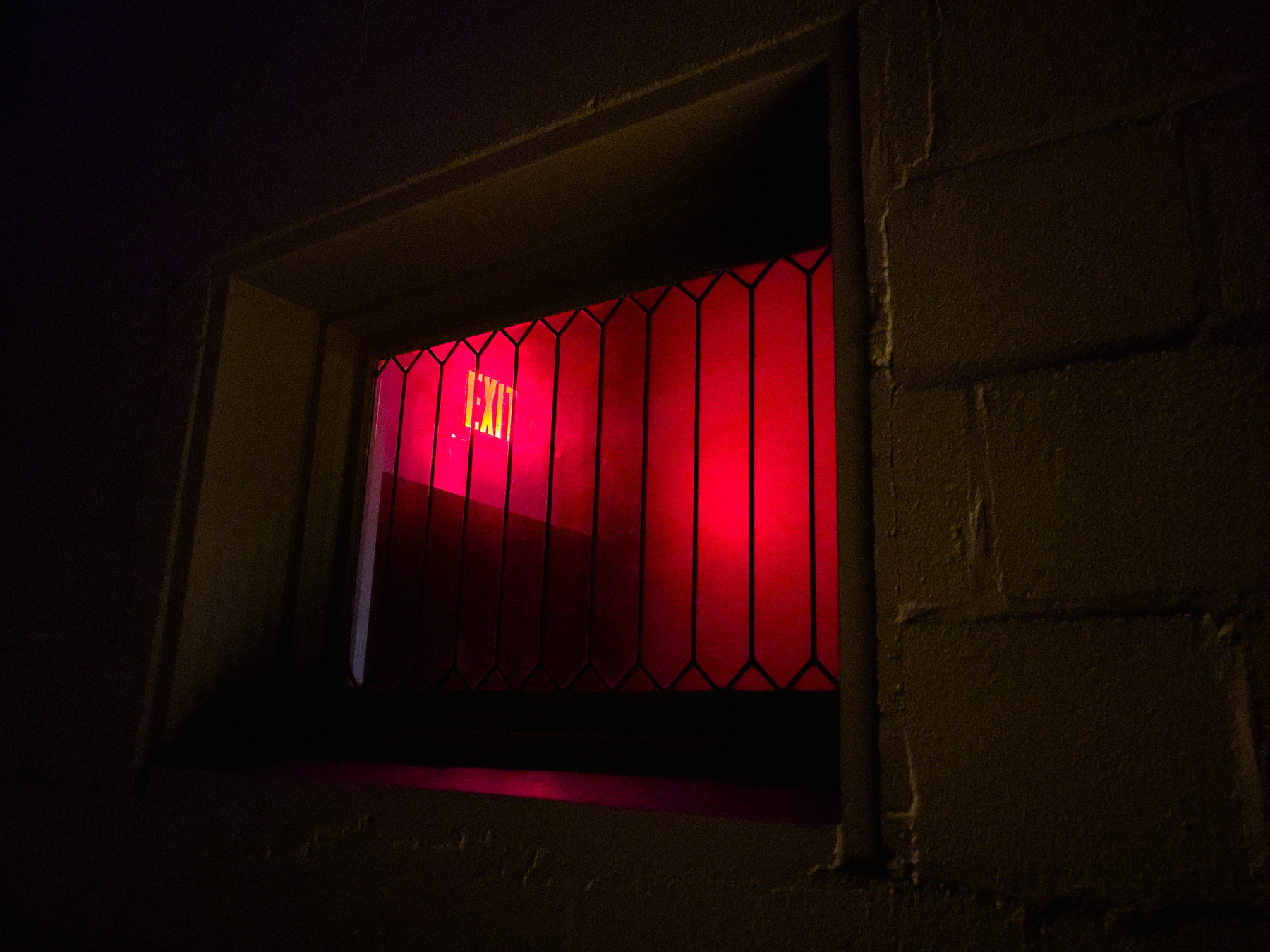 Red illuminated exit sign through a building window.