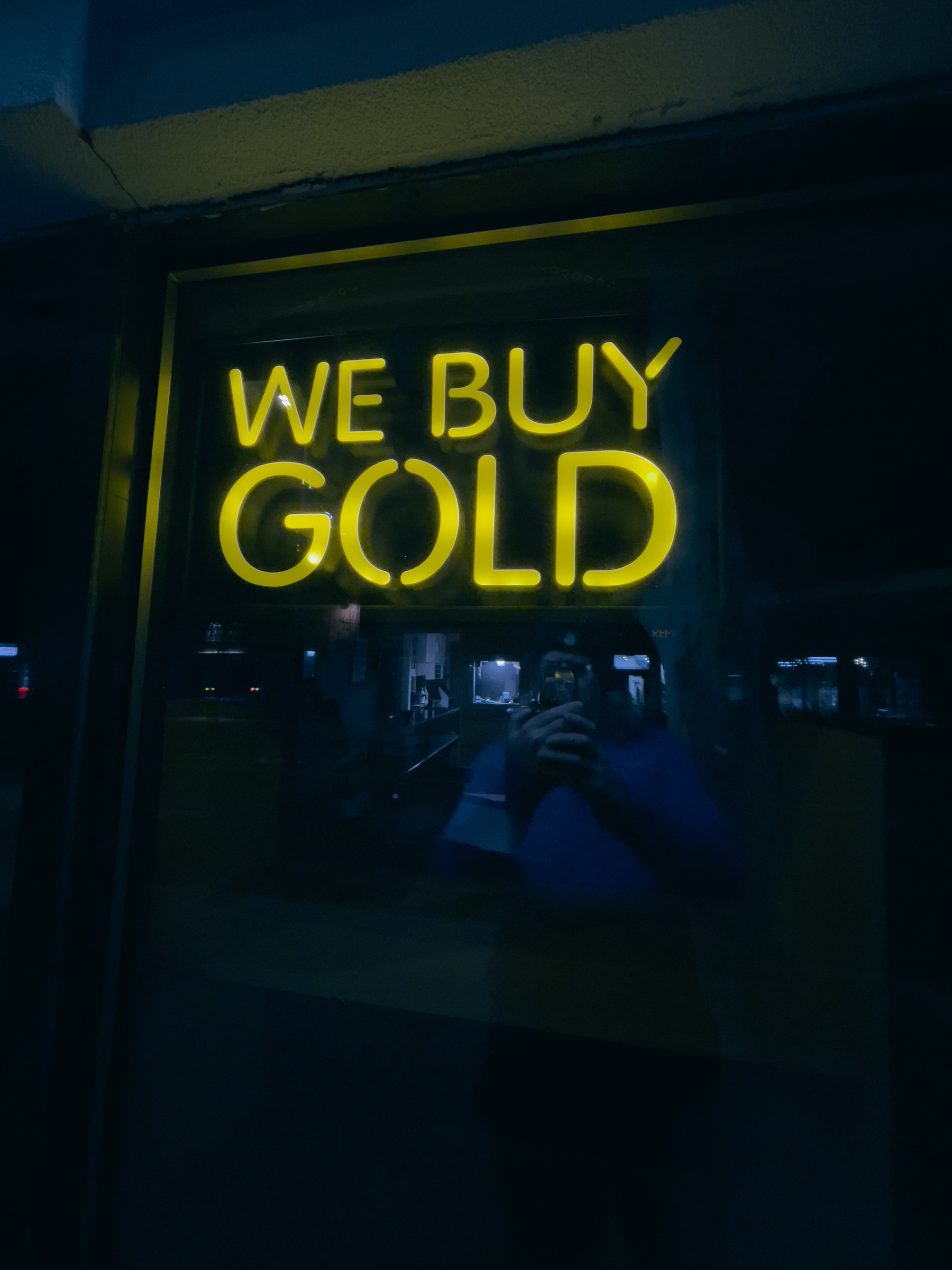 Illuminated “WE BUY GOLD” sign in shop window.
