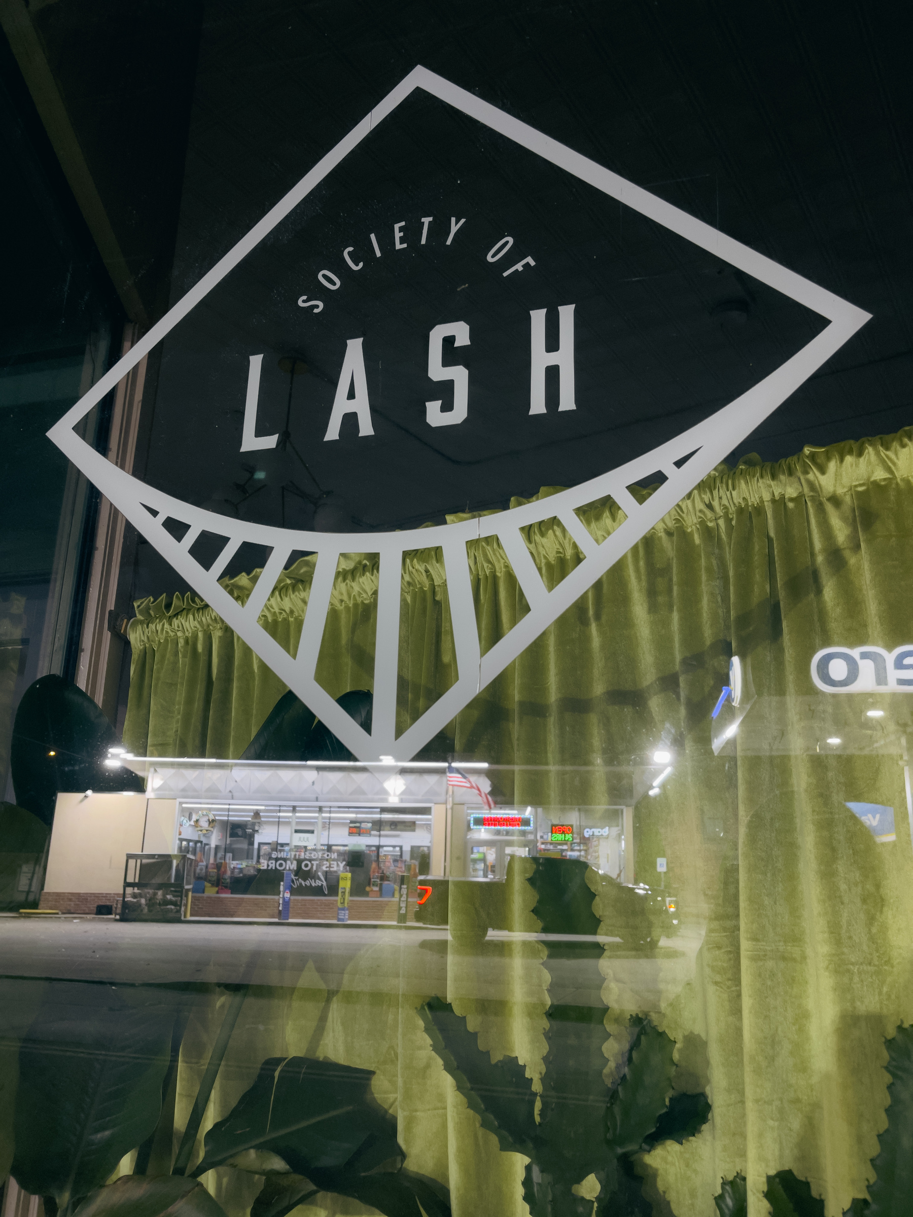 Society of Lash window graphic with gas station reflection overlaid.