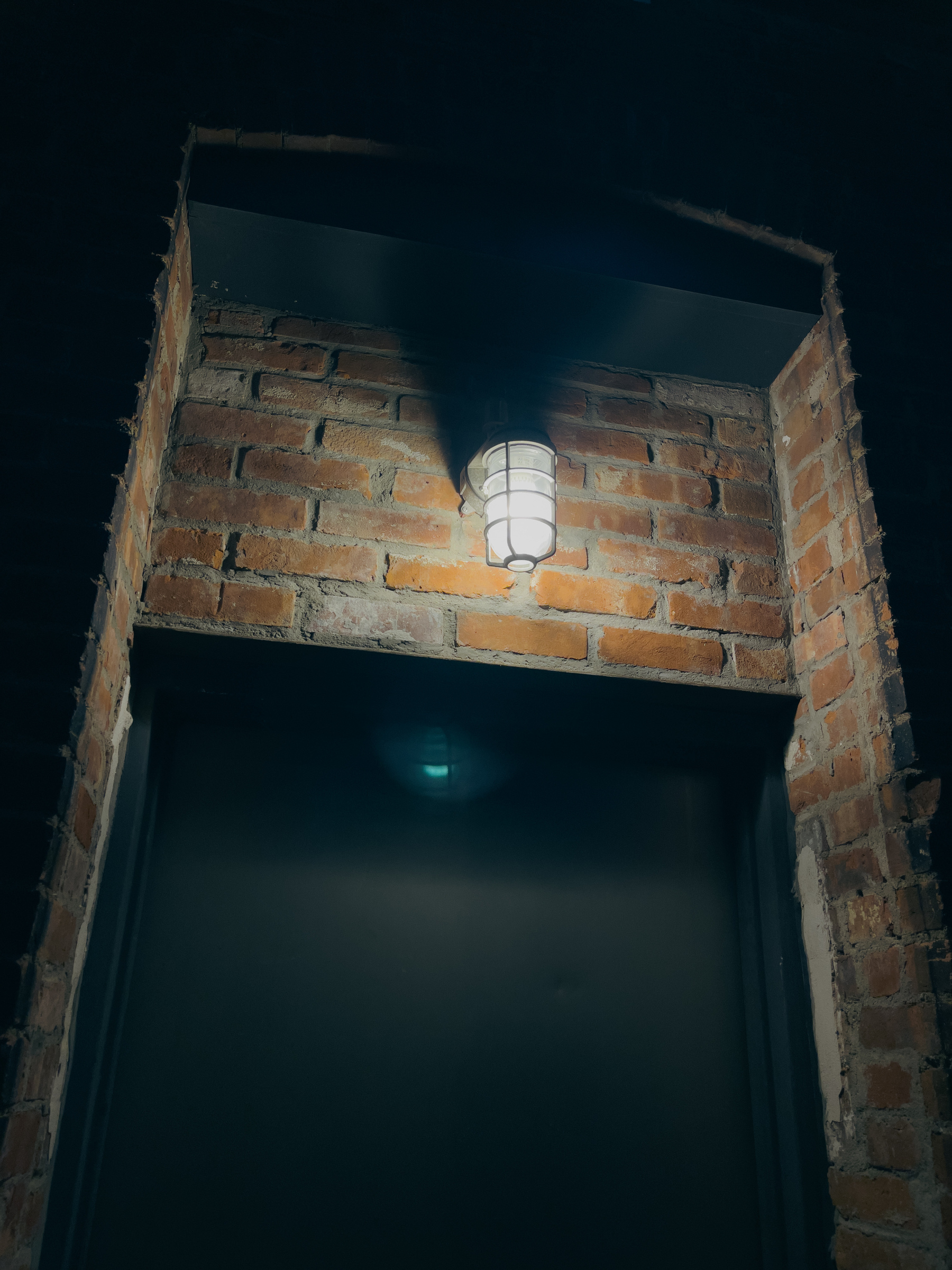 Door and light recessed into brick wall at night.