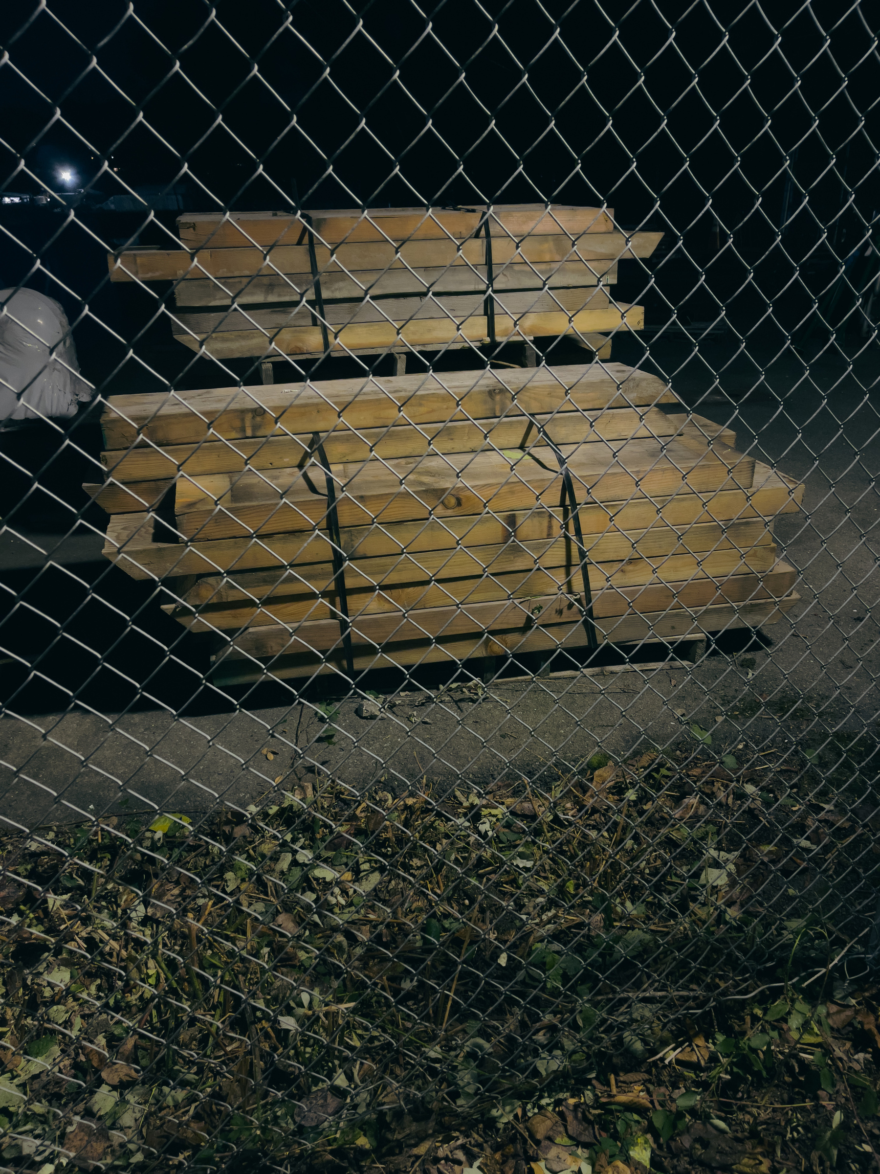 Heavy timber lumber stacked behind chain link fence.