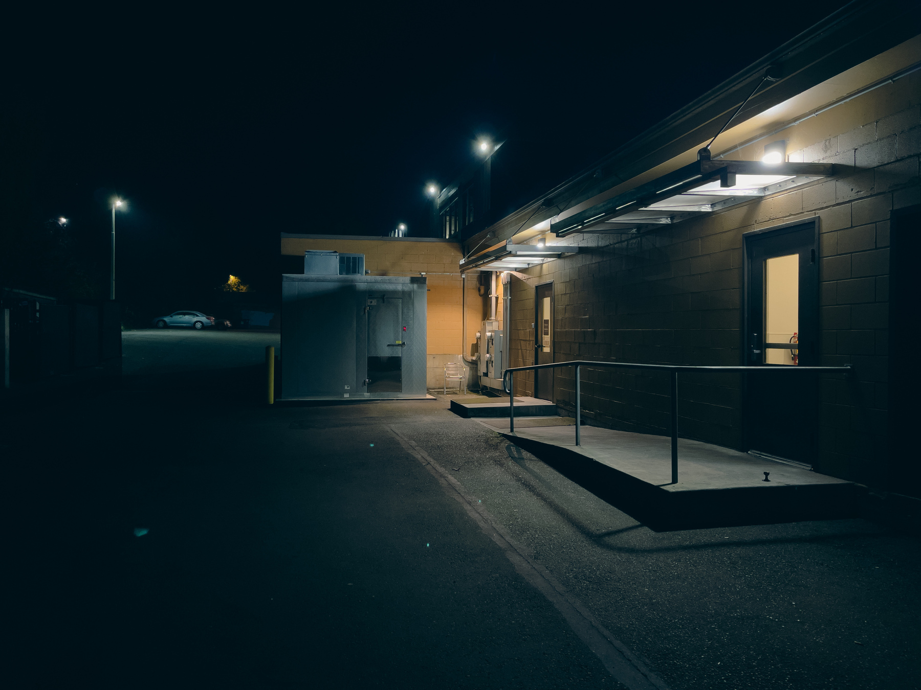 Alley behind commercial buildings lit by security lights.