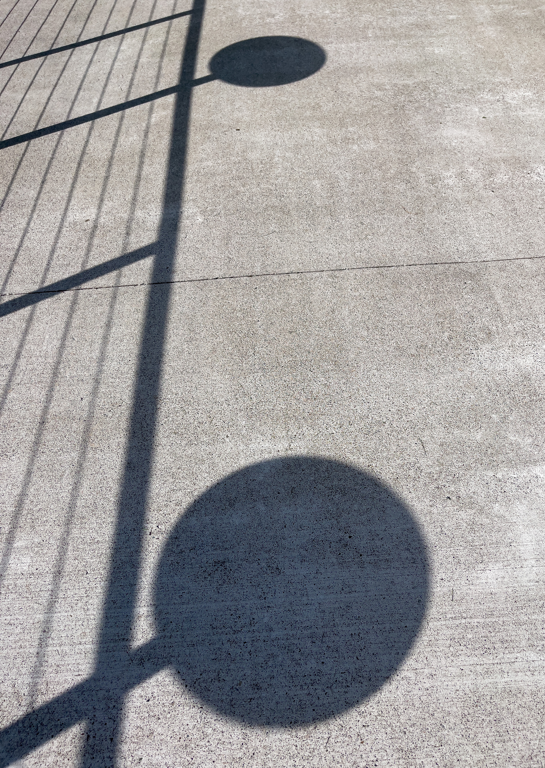 Shadow of railing and small circular tables on posts. Concrete terrace.