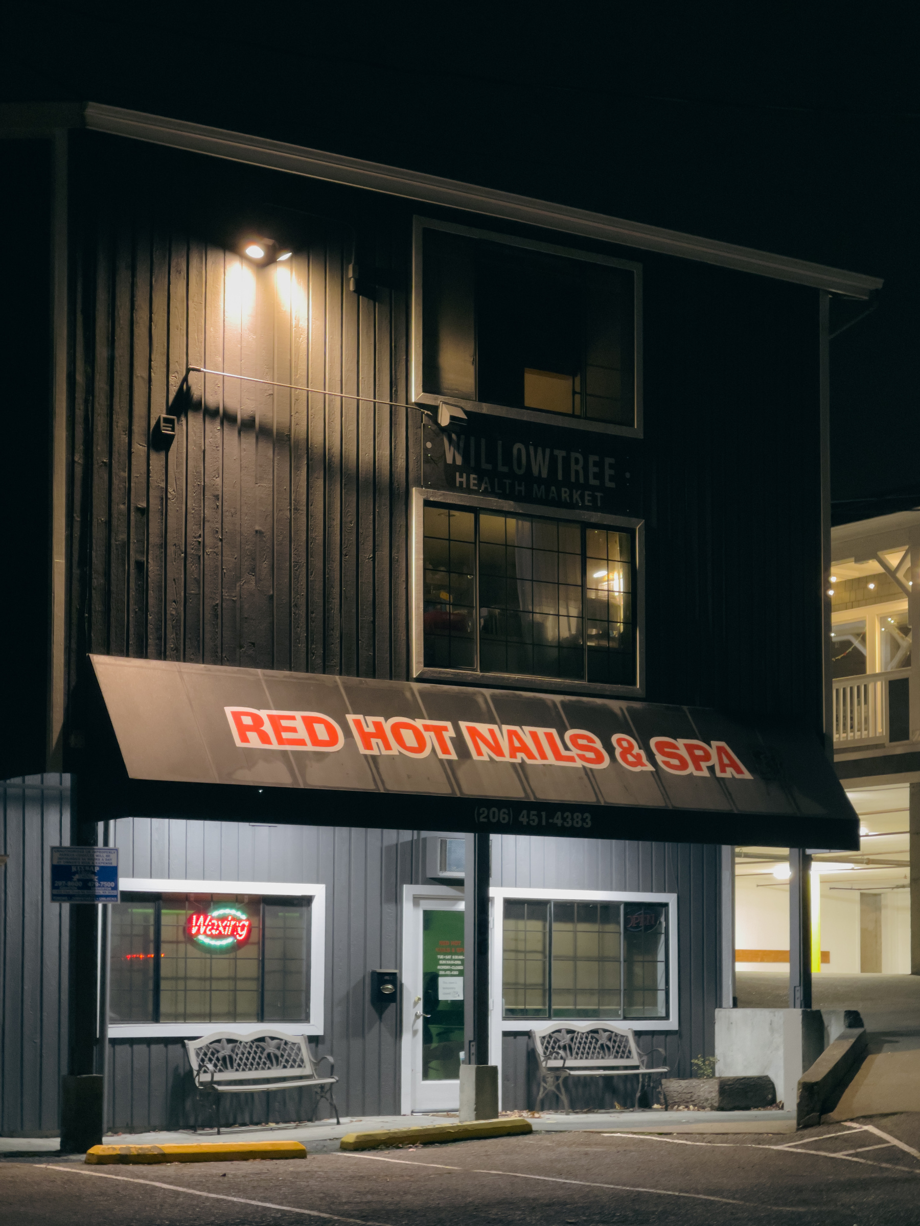 Three story commercial building with Red Hot Nails Salon on the ground floor at night.