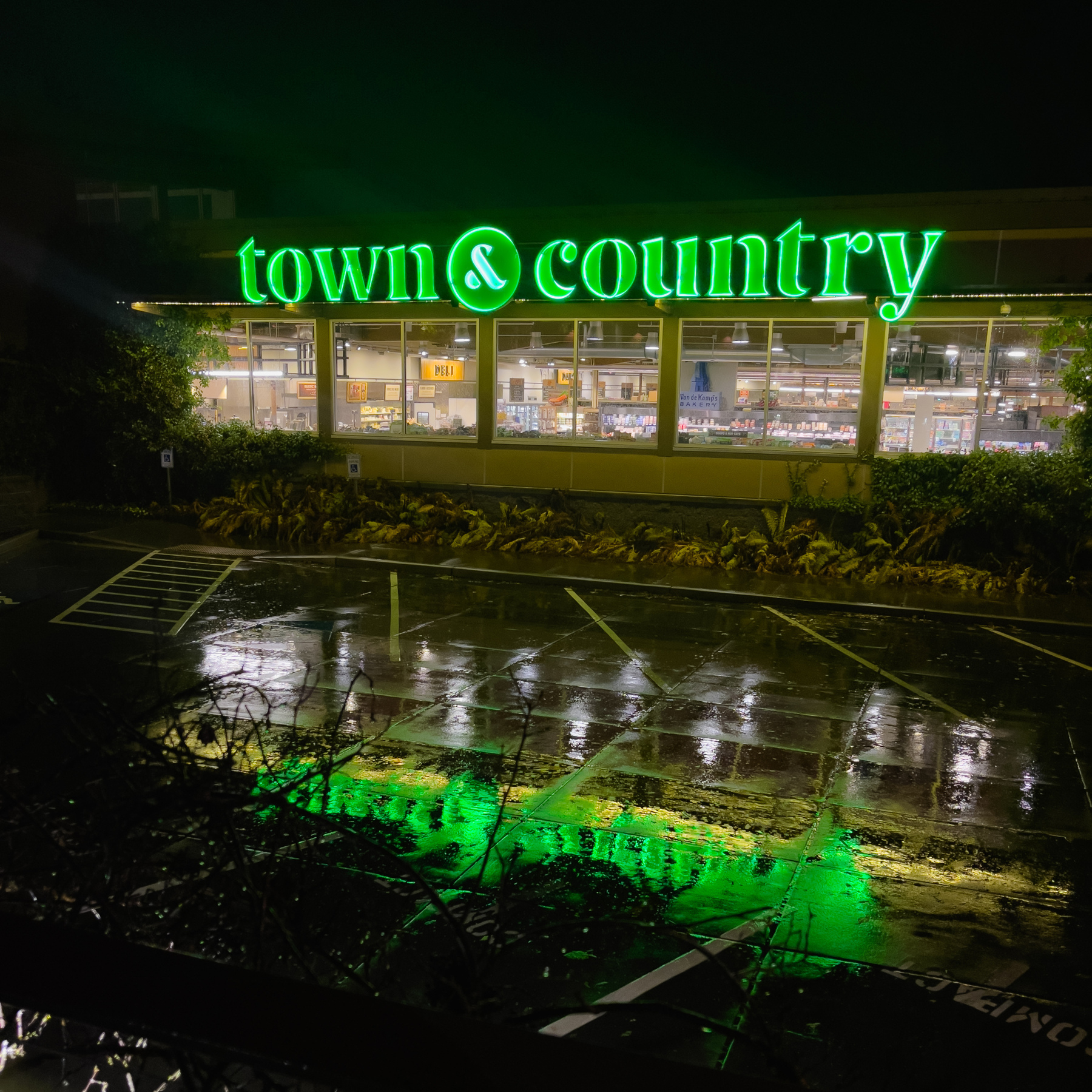 “Town &amp; Country” supermarket neon signage at night reflected in wet parking lot pavement below.