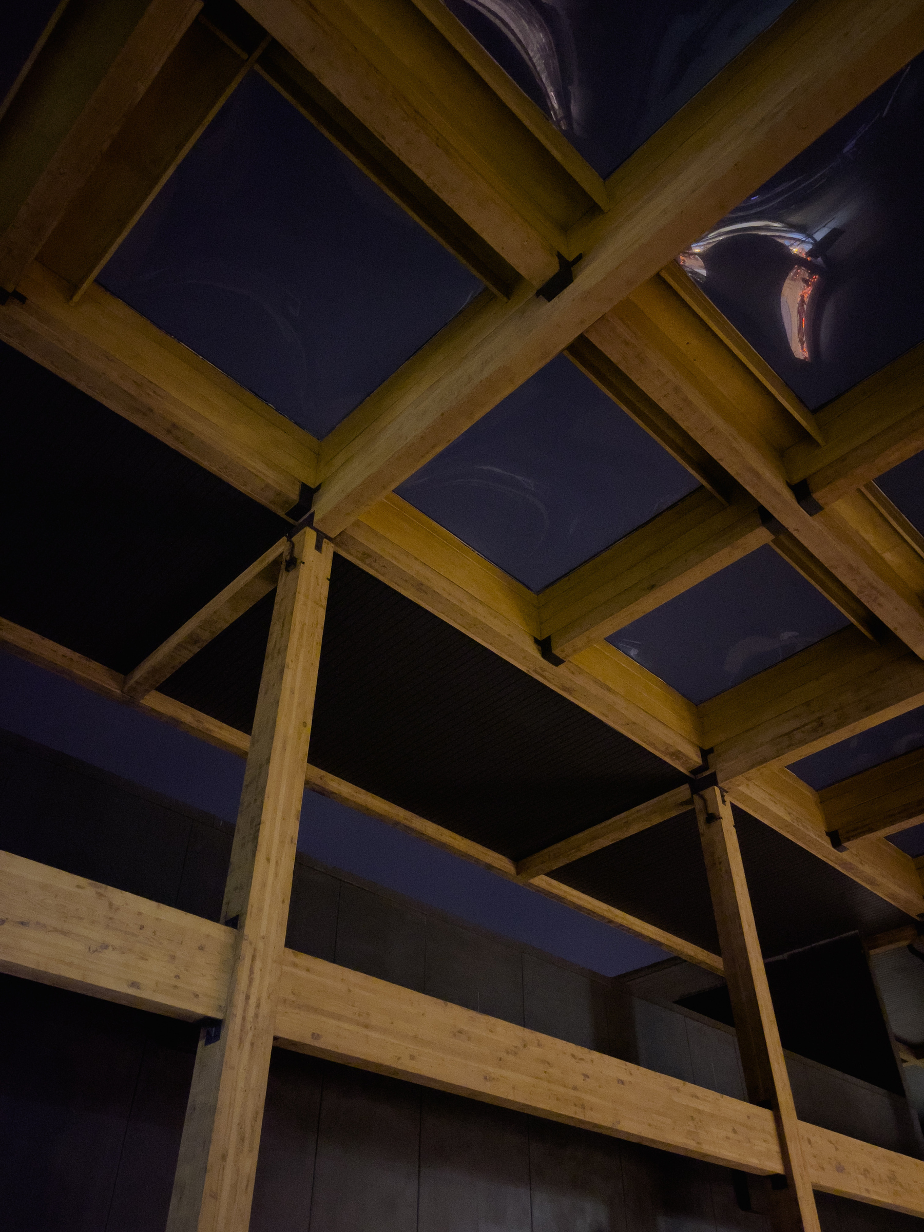 Timber frame skylight and support structure in outdoor atrium, lit by security lights 