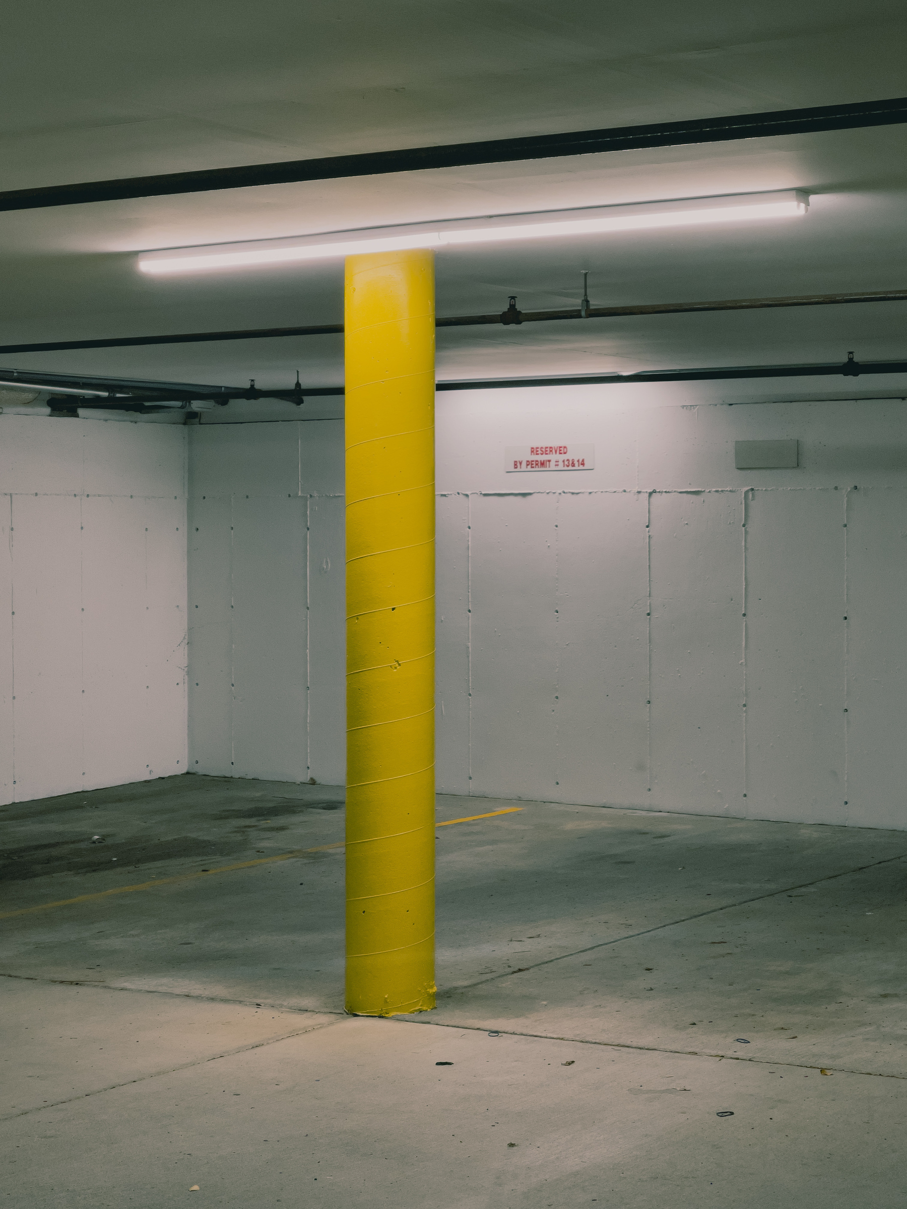 Corner of a parking garage with column painted yellow and fluorescent striplight fixture illuminating the scene.