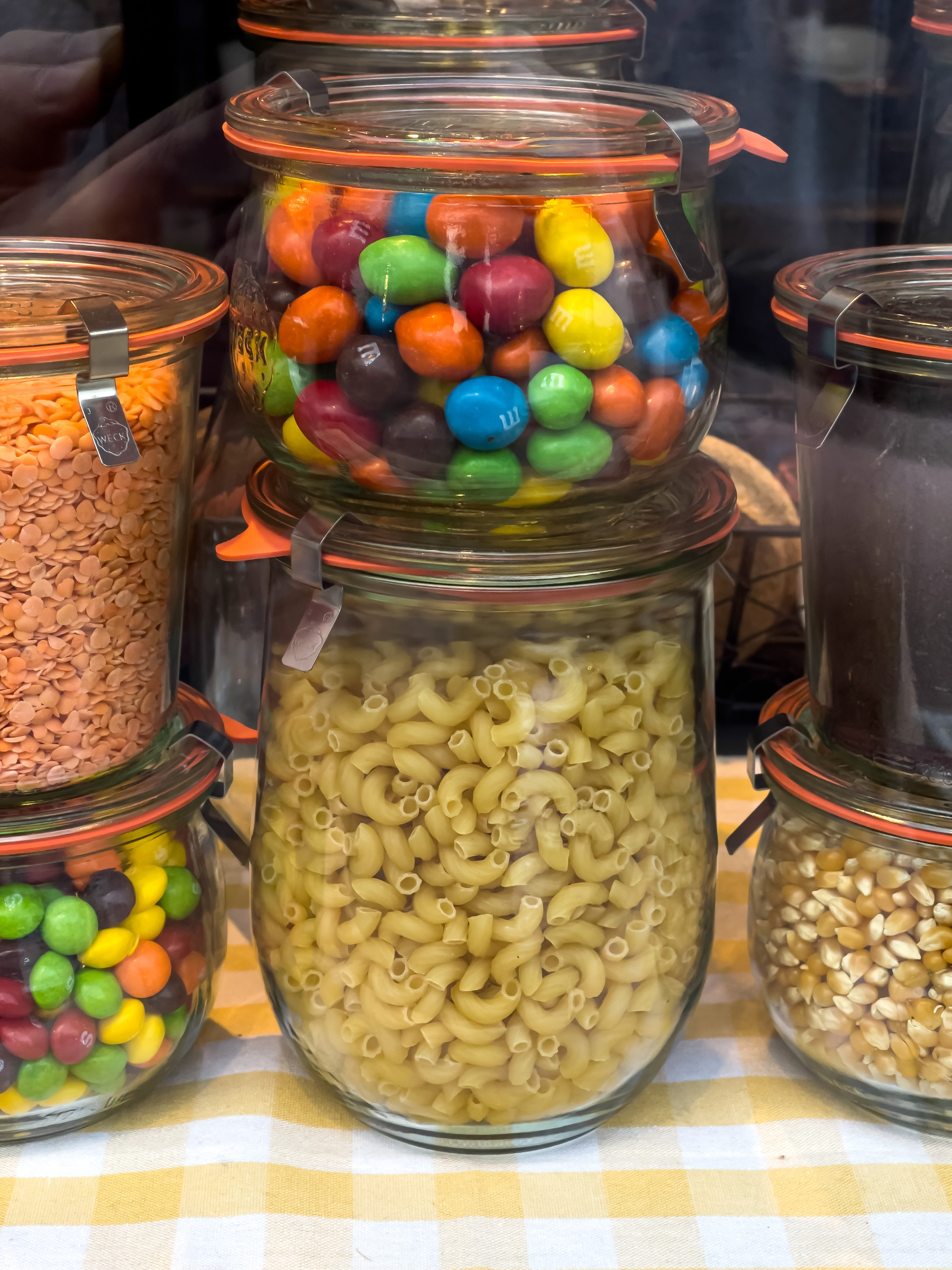M&amp;M candies and macaroni in glass storage jars in a shop window.