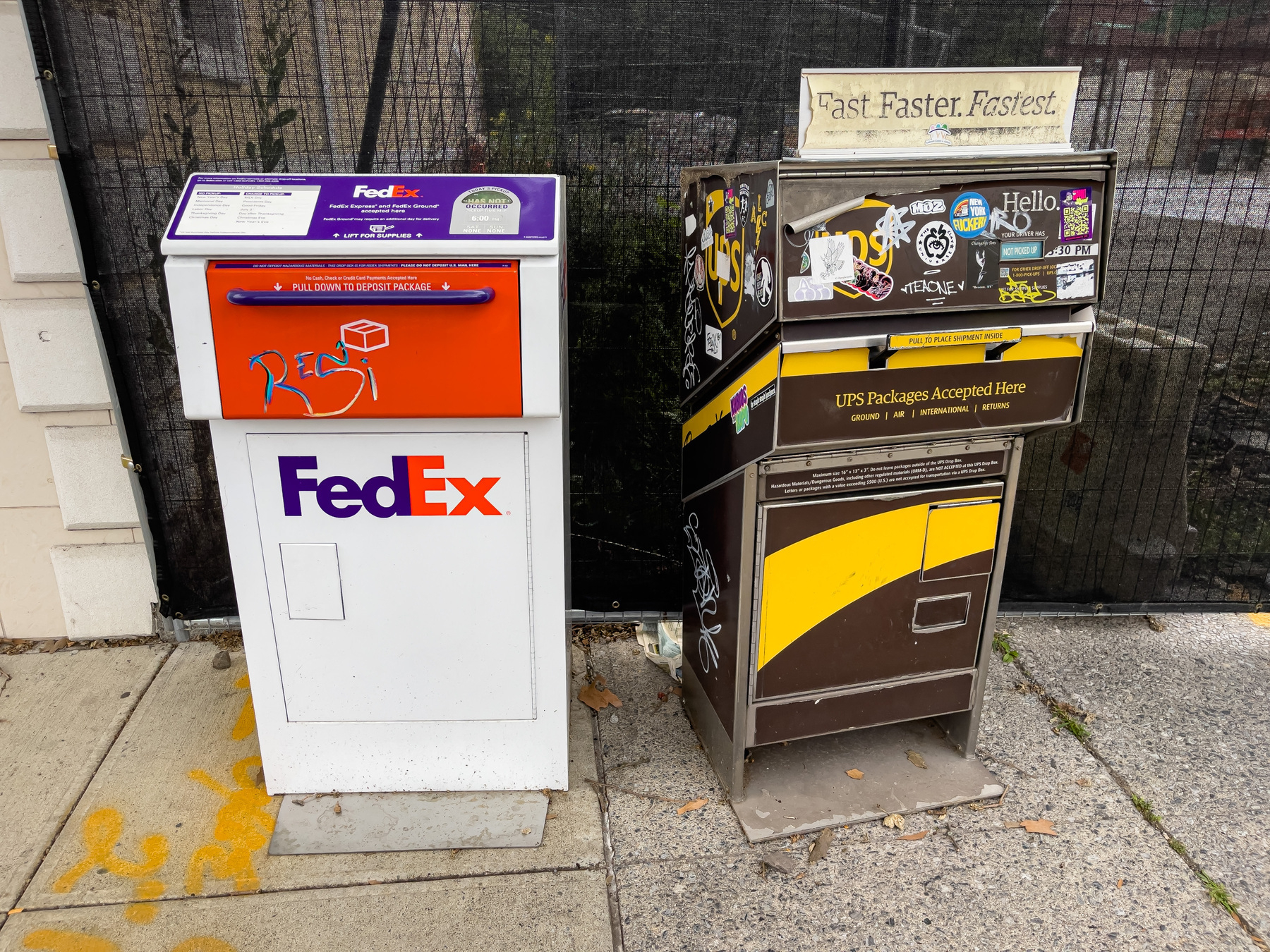 FedEx and UPS drop boxes on sidewalk in front of construction site.