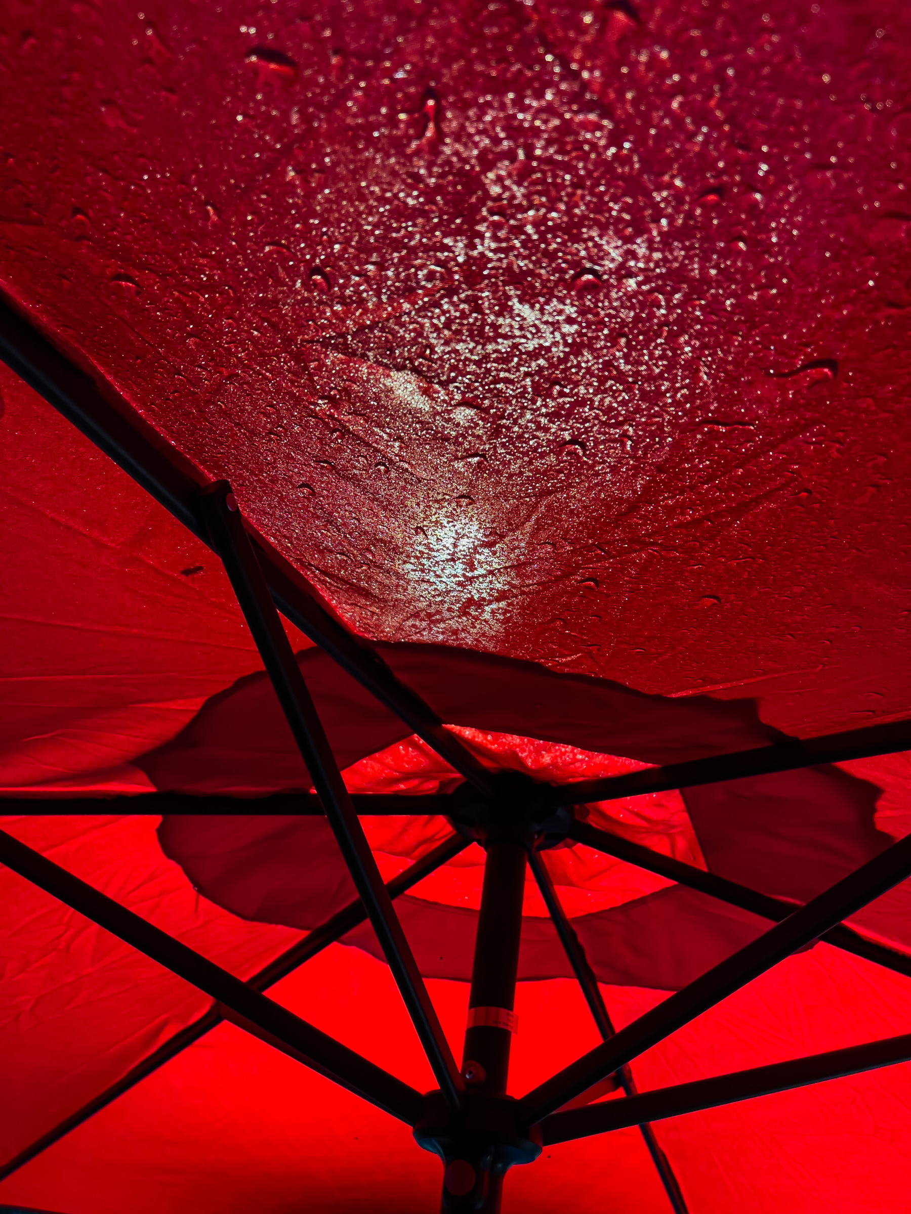 Underside of red umbrella with streetlights shining through at top of frame revealing water droplets sitting on top.