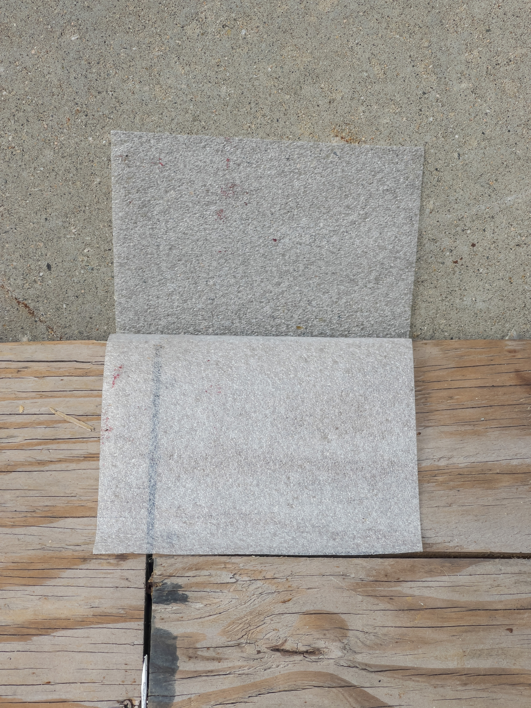 rectangular paper sheet laying on top of plywood and against concrete barrier
