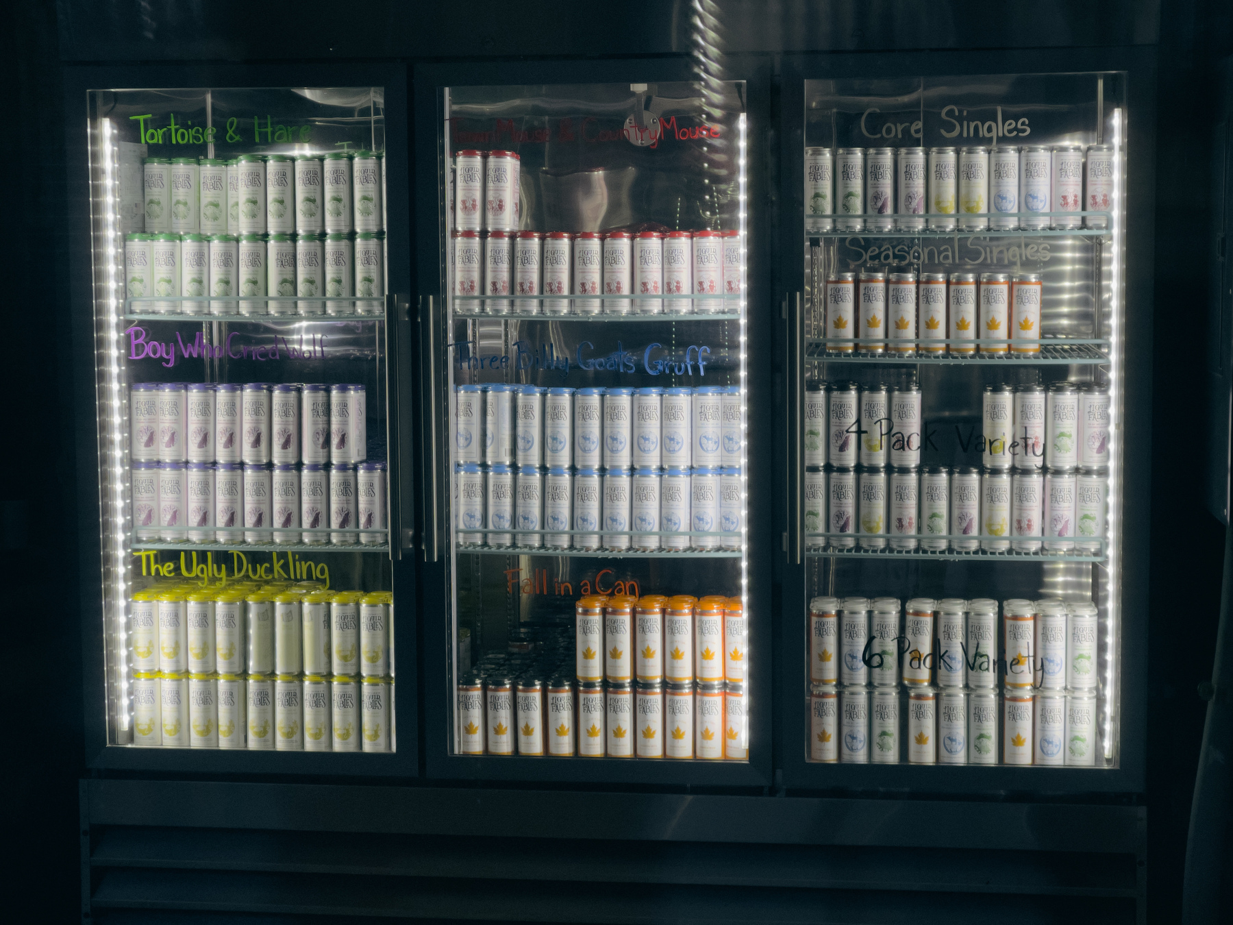 Three drink refrigerators with glass doors, lit from within and filled with canned beverages.