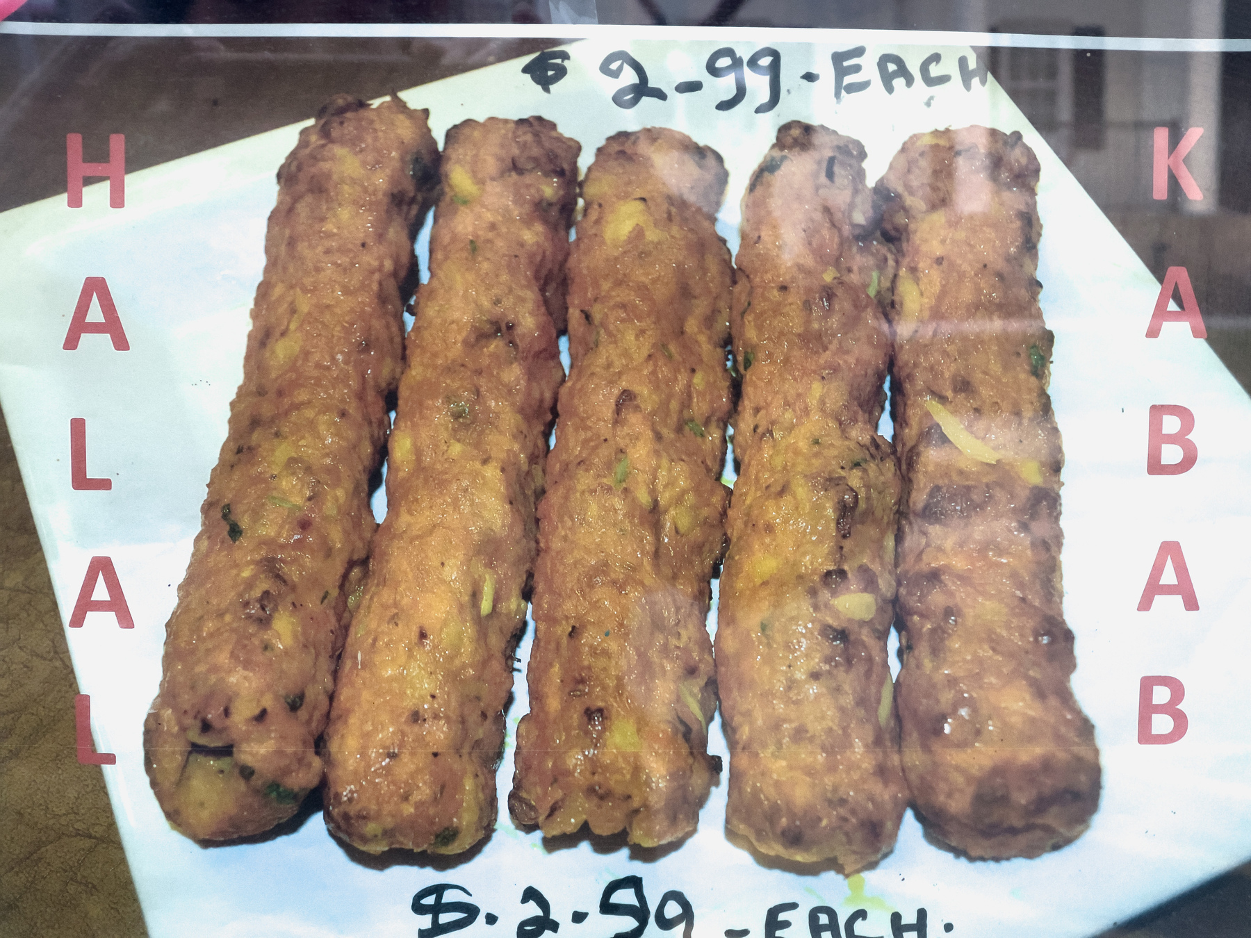Halal Kabab poster in restaurant window showing 5 kababs and price of $2.99 each.