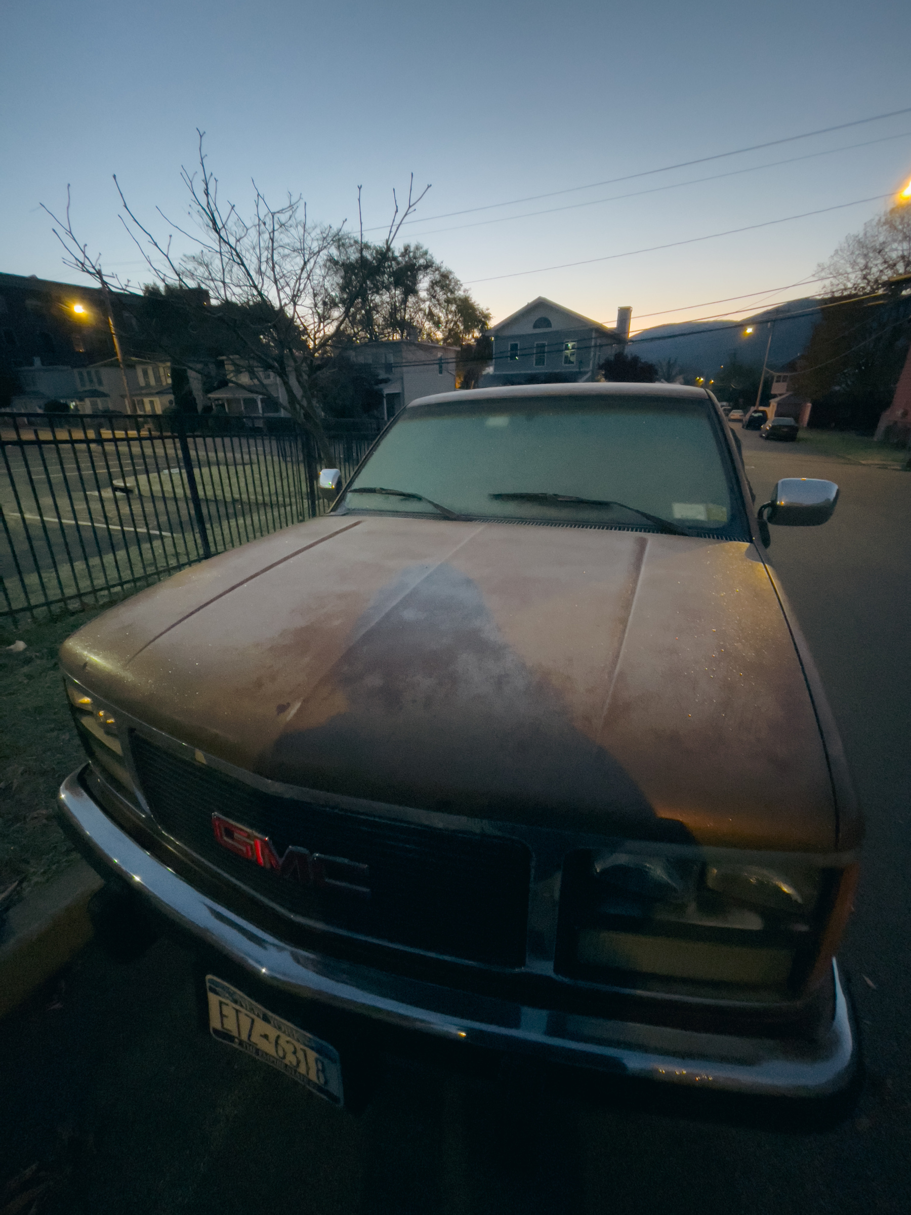 Wide angle view of old pickup truck with frost on hood and windshield and dawn sky in distance.