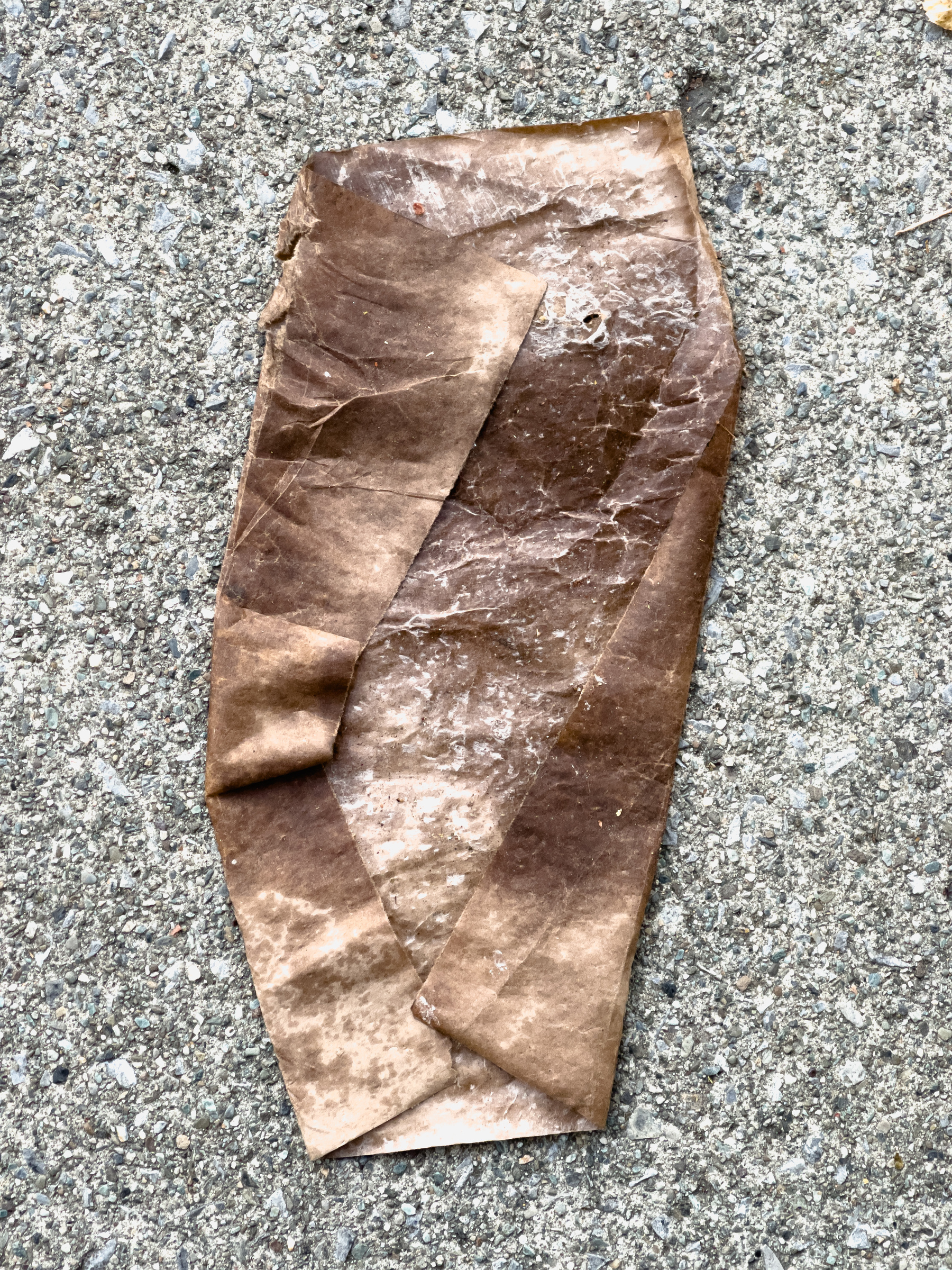Brown wax paper folded in an interesting way on concrete sidewalk.