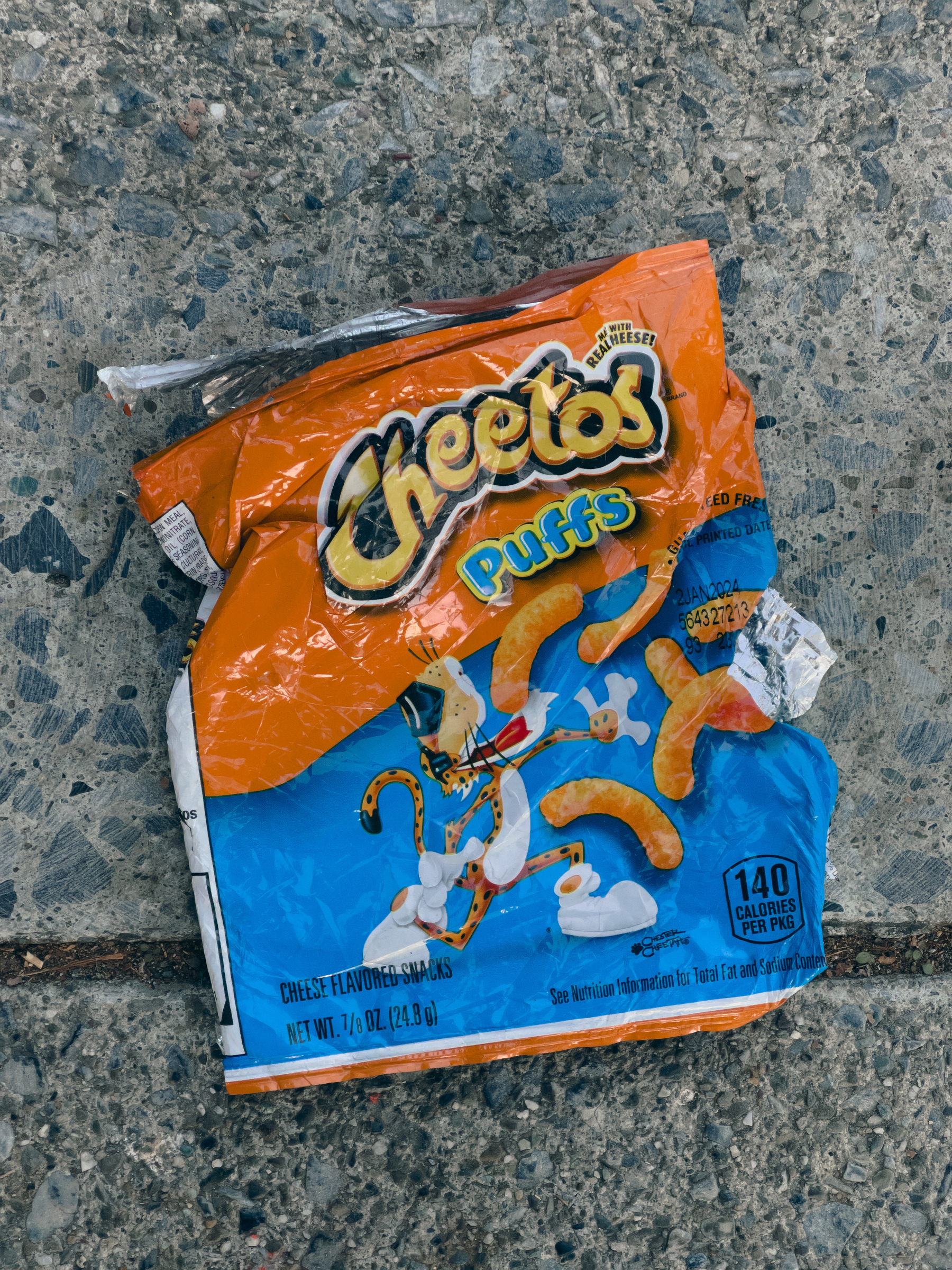 Cheetos Puffs bag lying on concrete sidewalk.