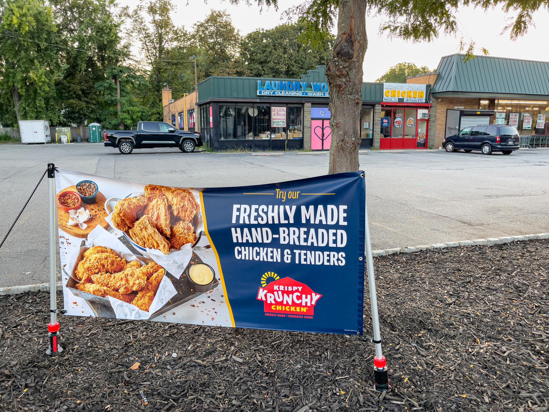 Temporary banner sign advertising Krispy Krunch Chicken shop in commercial strip mall beyond.