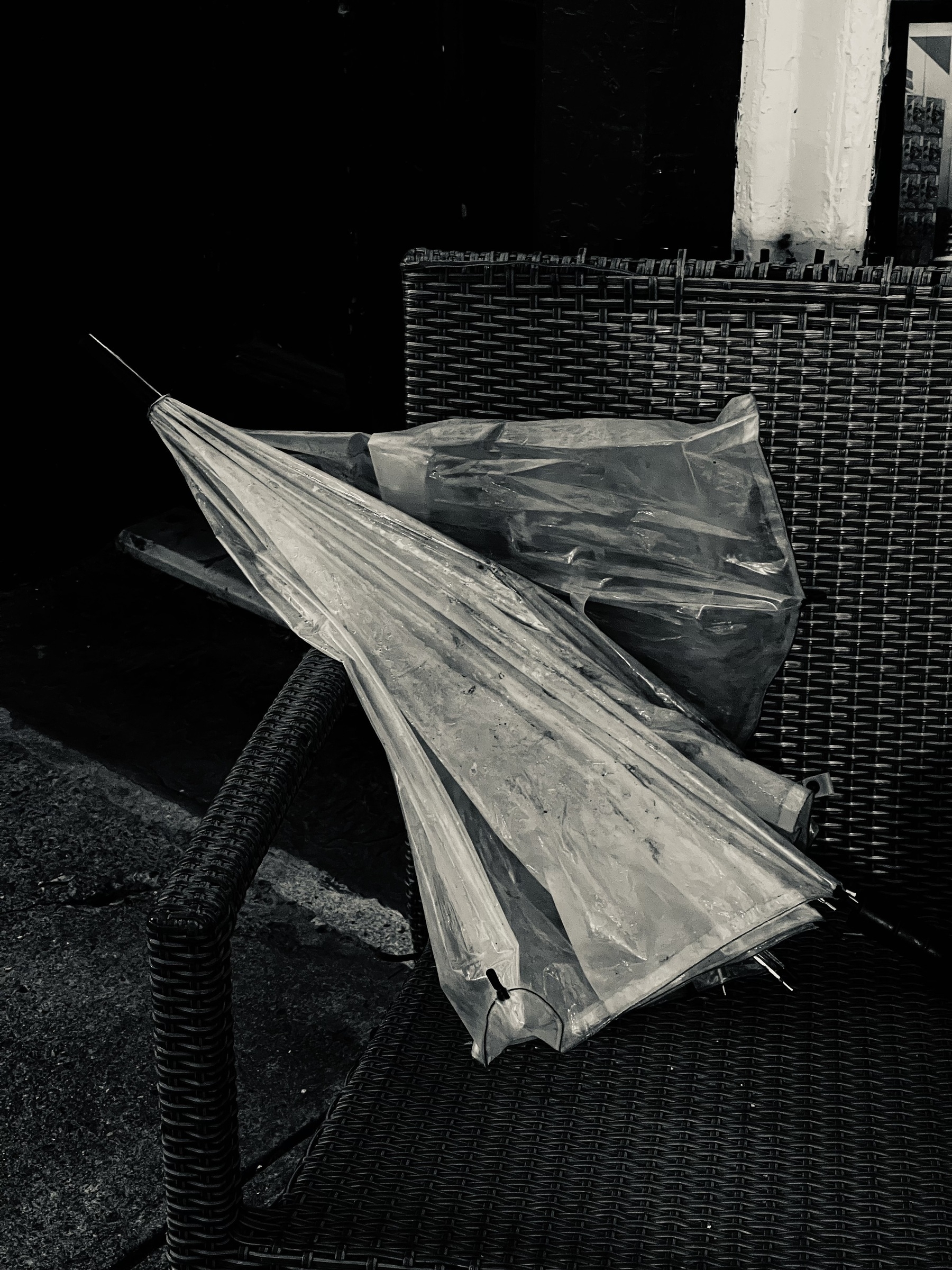 Transparent, folded, umbrella on a wicker chair.