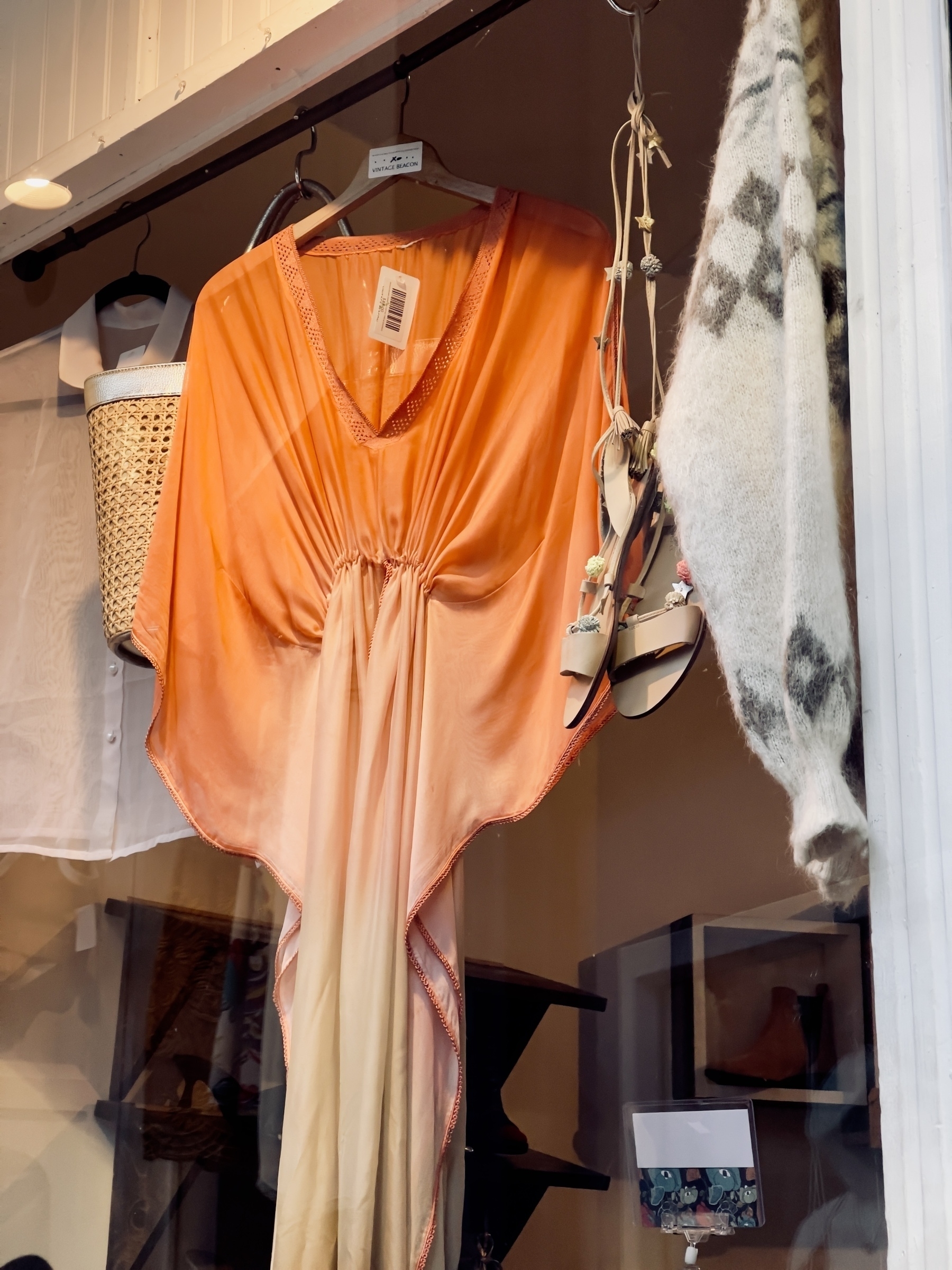 Silky orange evening dress, with gathered waist, hanging in a vintage clothing shop window.