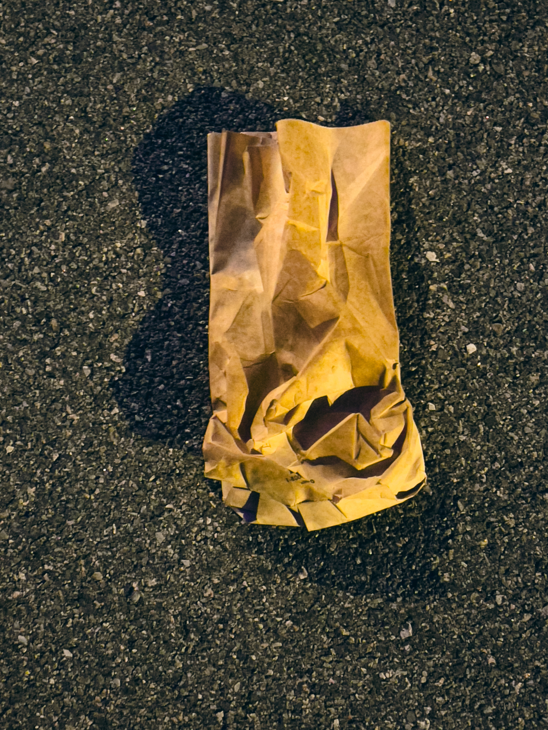 Crumpled brown paper bag on asphalt pavement illuminated by streetlights.