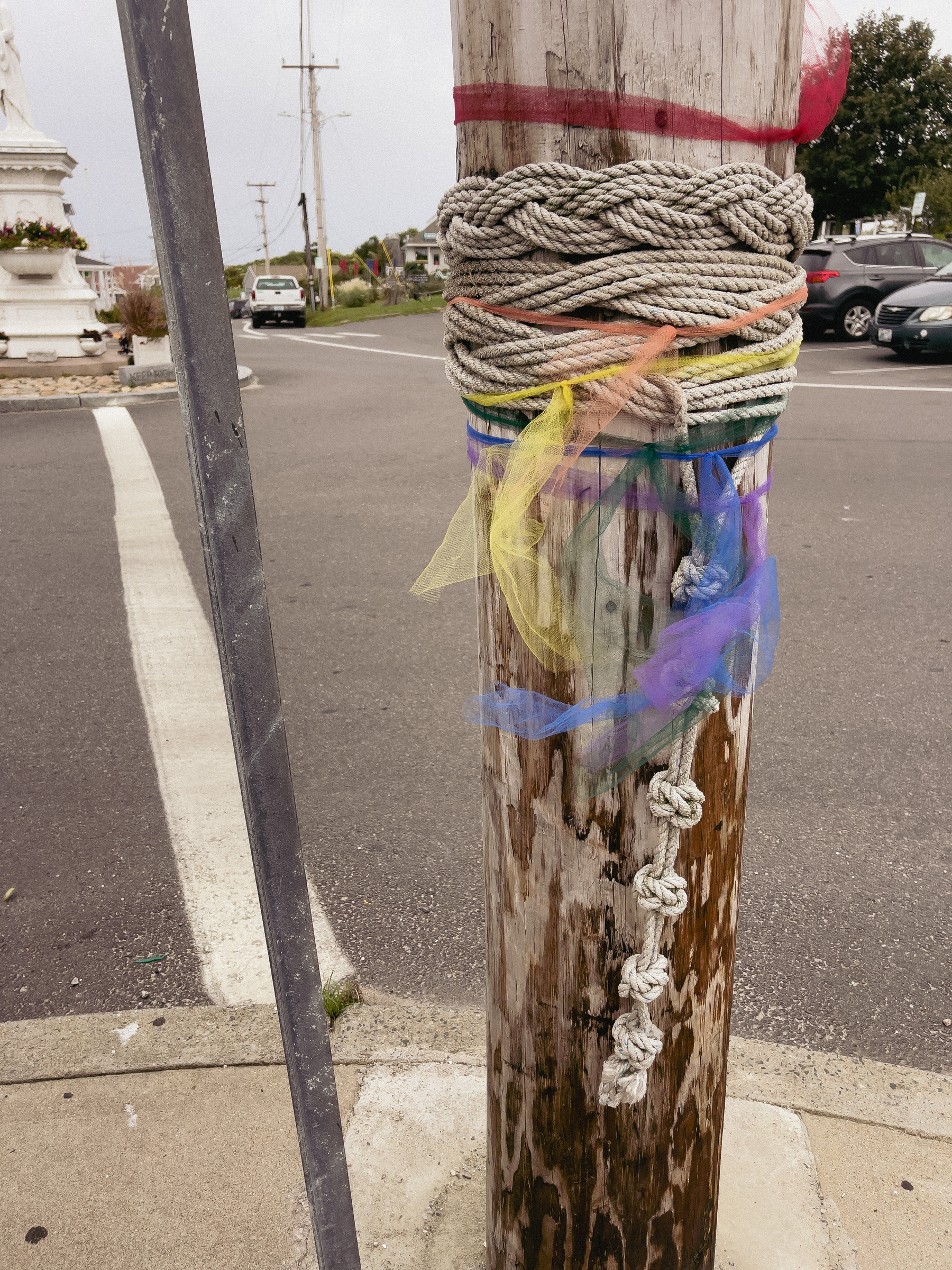 Nautical rope weaving around telephone pole. Gauzy red, yellow and blue gay pride fabric tied over rope.