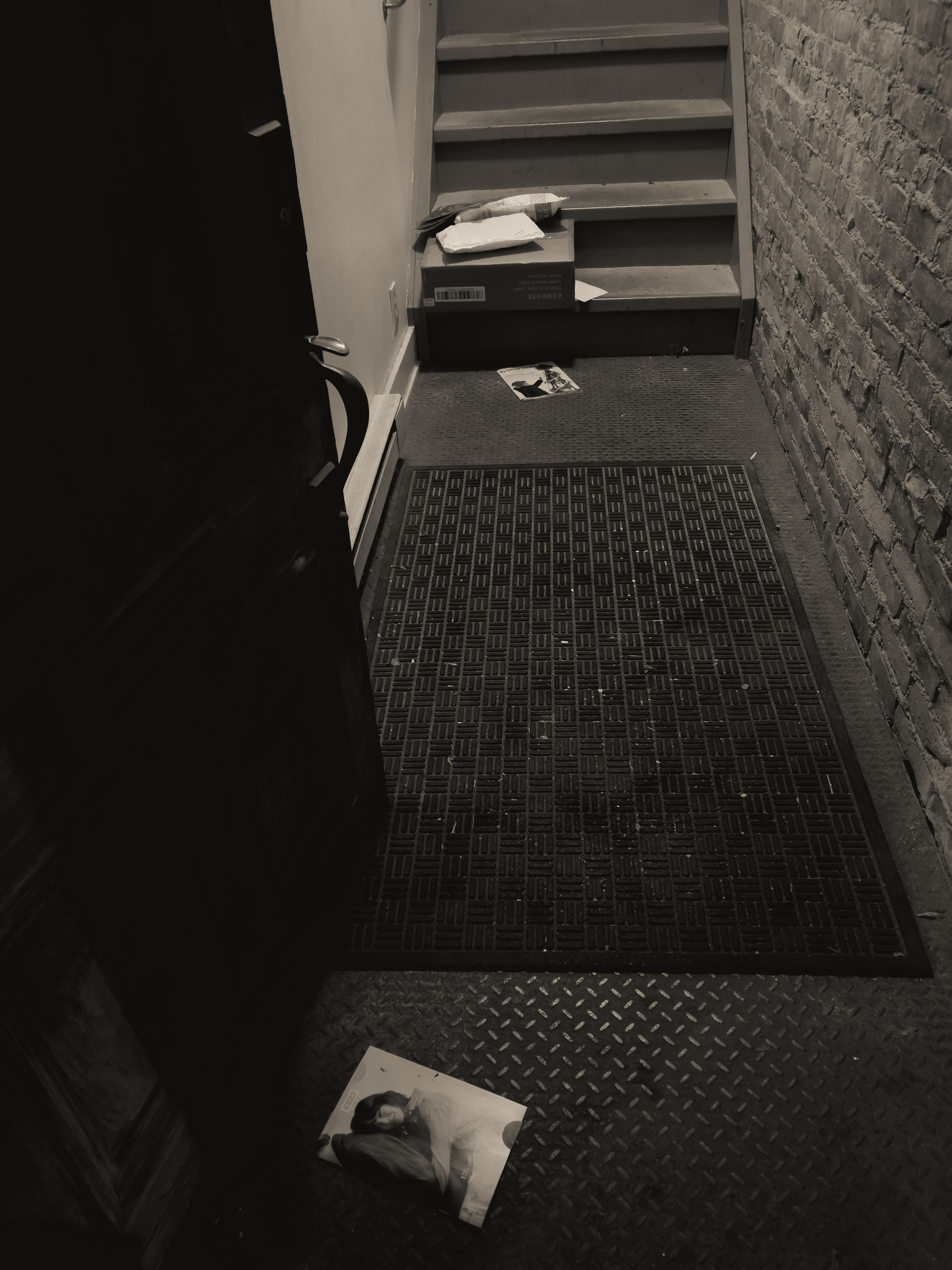 Entryway to apartment building with mail and packages strewn on the floor and stairs to upper floors in background.