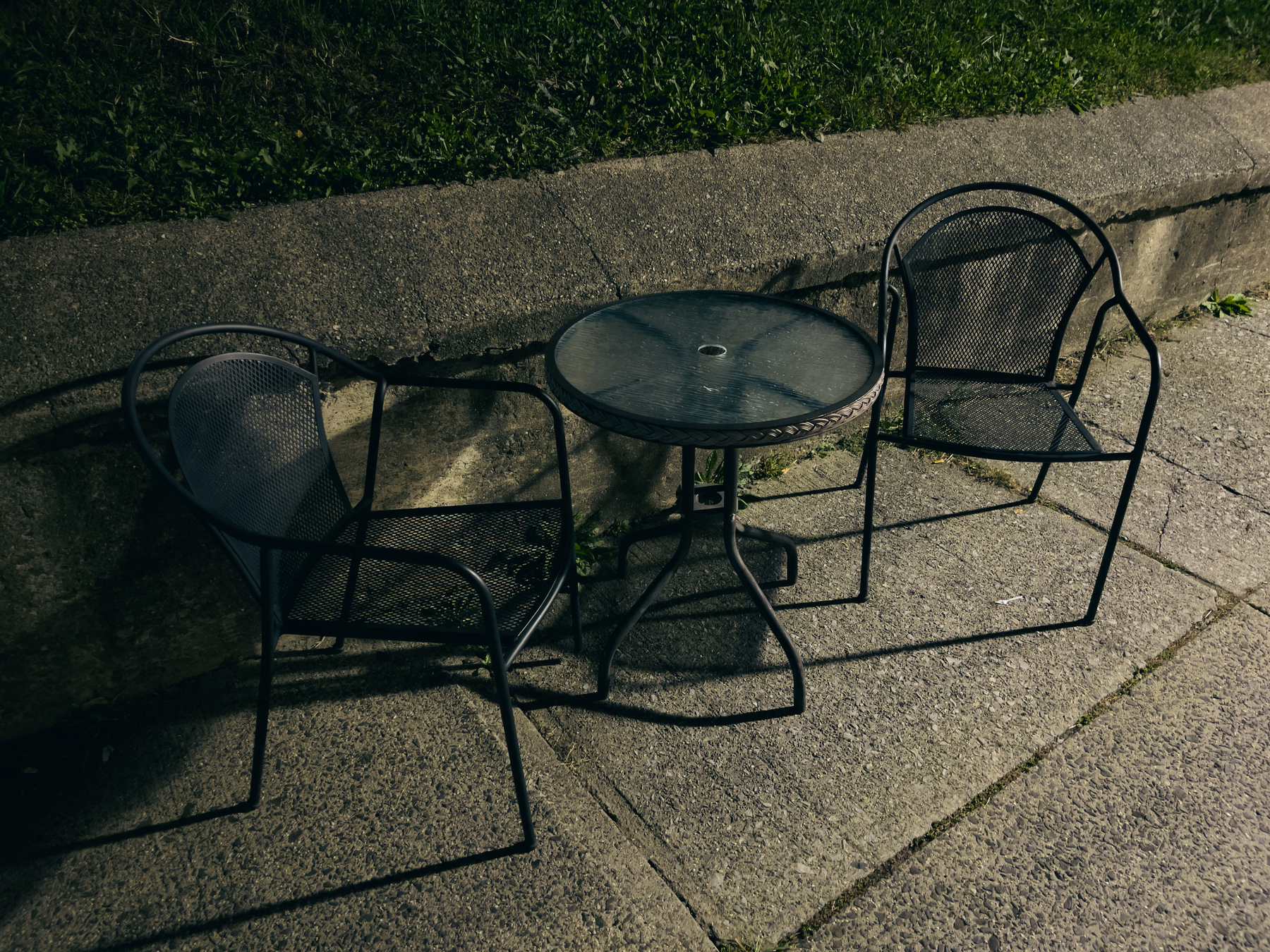 Metal table and chairs on sidewalk next to a retaining wall. 