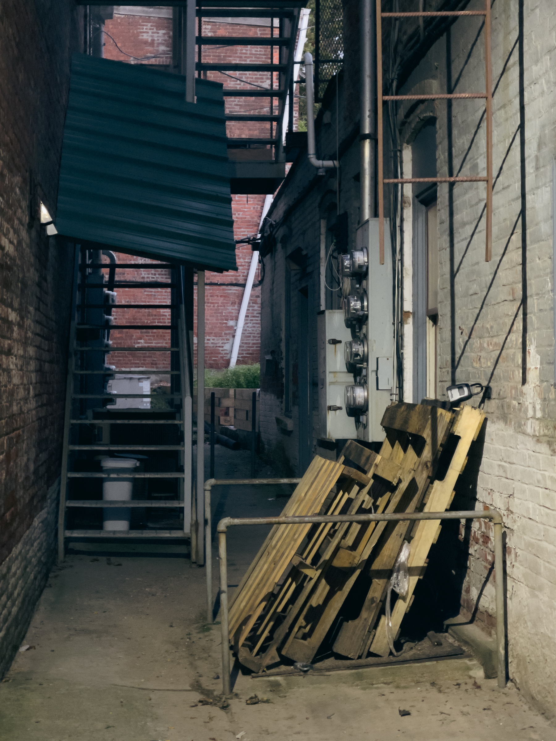 Alley between buildings wit fire escapes and wooden pallets.