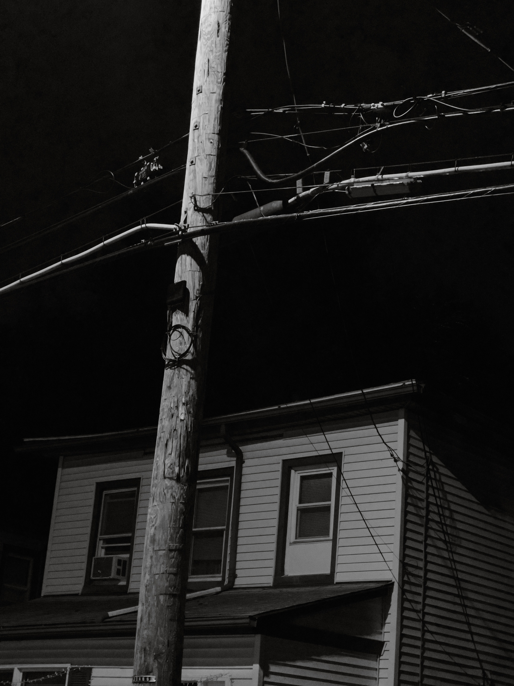 Wires, utility pole and upper part of house lit by streetlights.