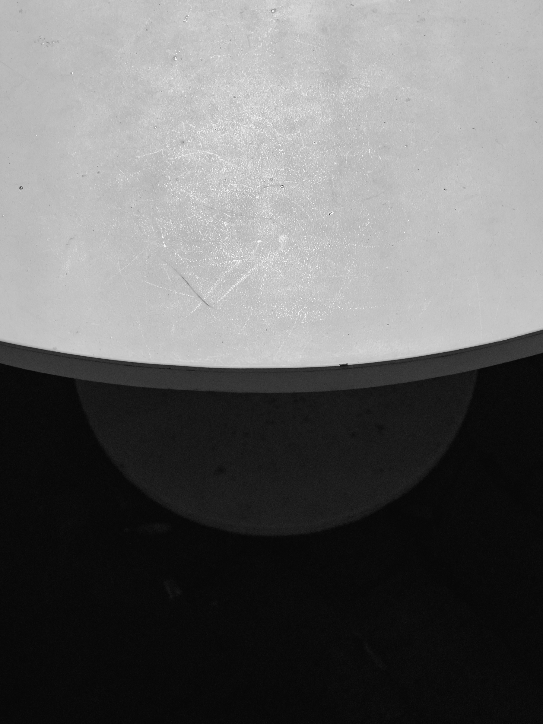 Closeup of edge of circular table with circular base in shadow below.