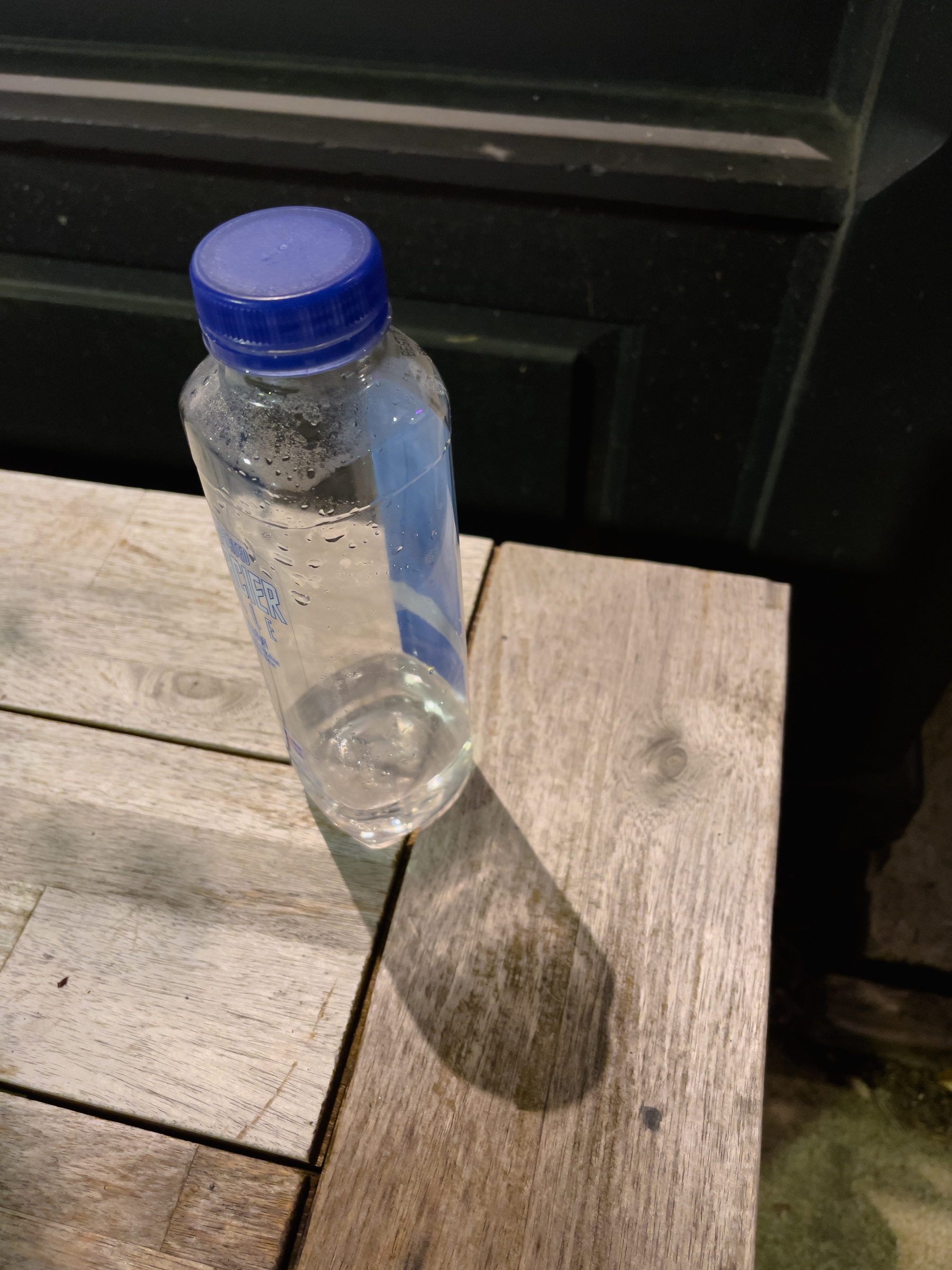 Plastic water bottle on a bench outside a shop window, shop lights illuminating it.