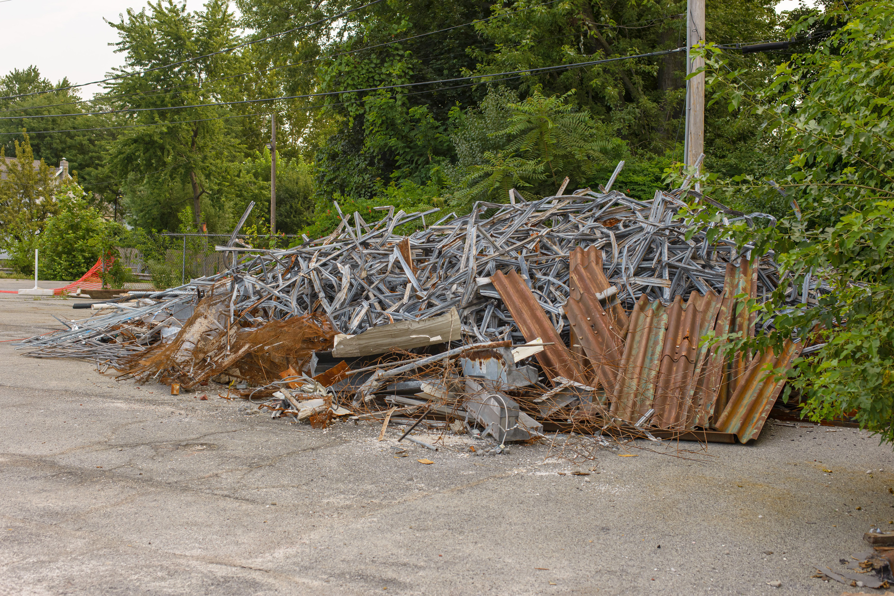 pile of metal demolition debris on asphalt surface with trees and weeds in the background