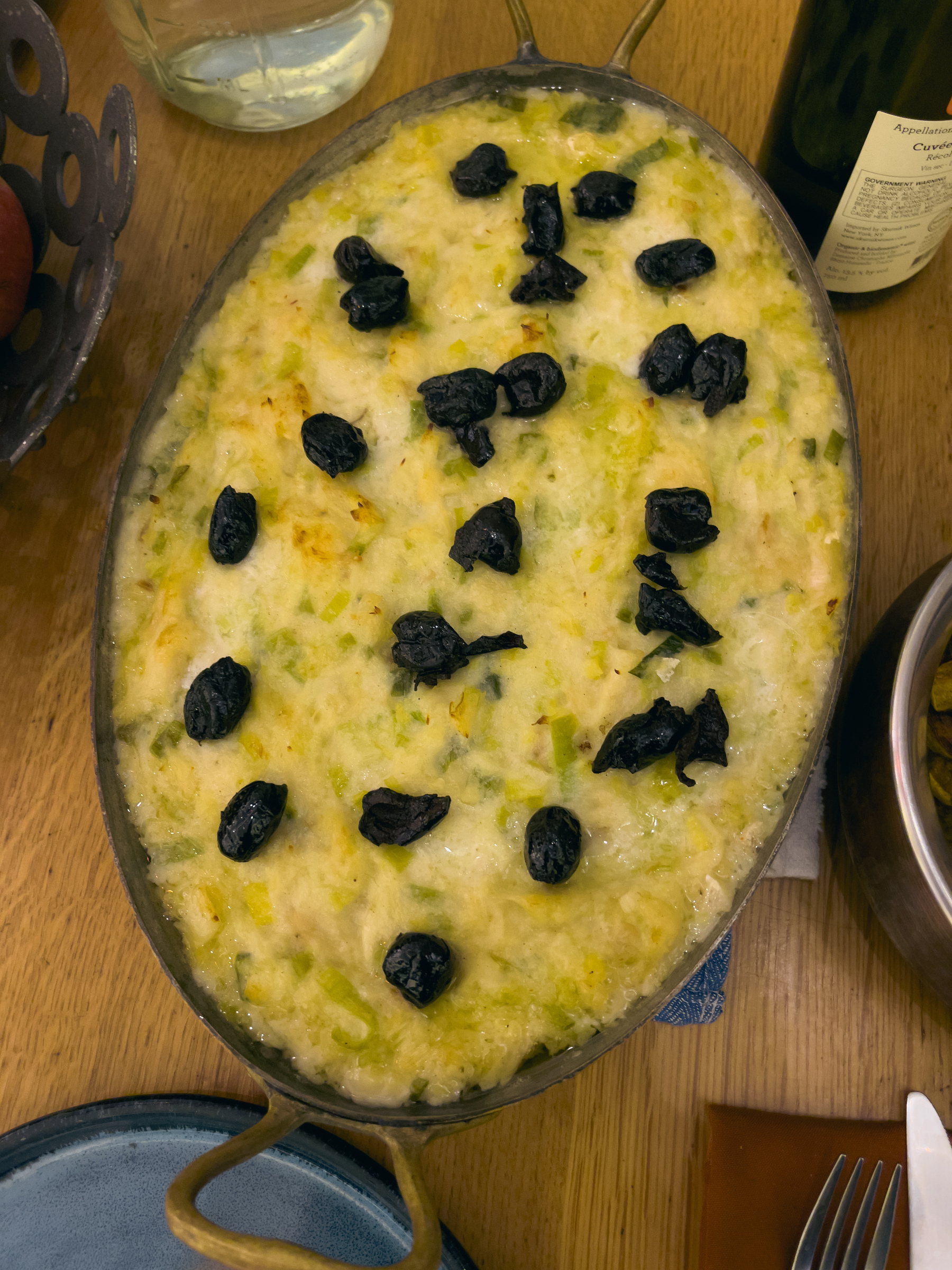 Completed salt cod and leek gratin dotted with oil cured olives in an oval metal baking dish.