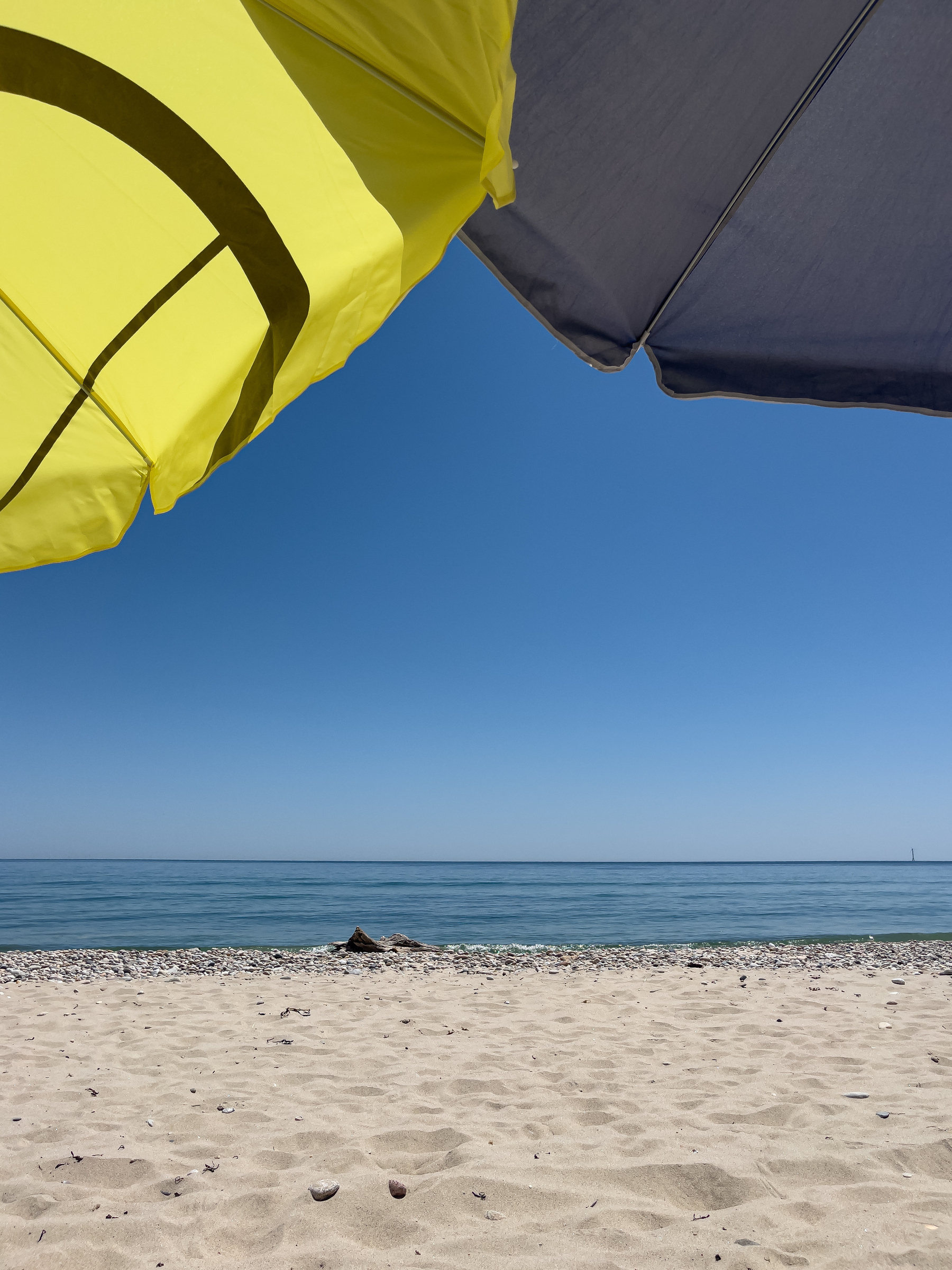 Ocean and beach with partial yellow and blue umbrellas at the top of the frame.