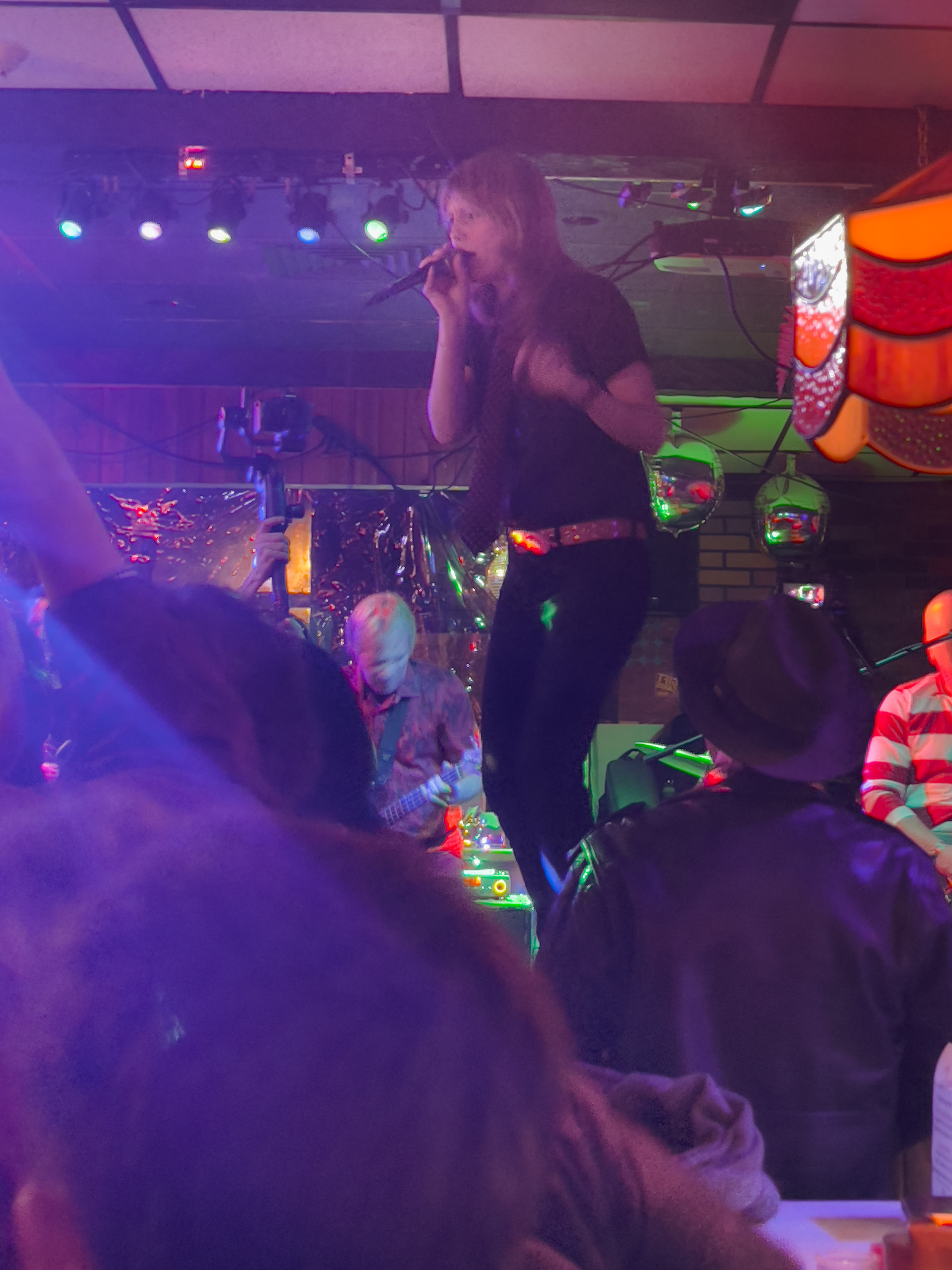 Woman singing into a mic at a bar surrounded by her fans.
