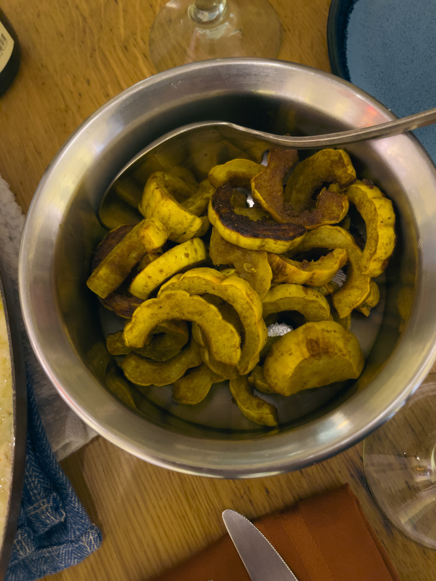 Half moon pieces of delicata squash roasted with curry powder. Served in a circular metal bowl.