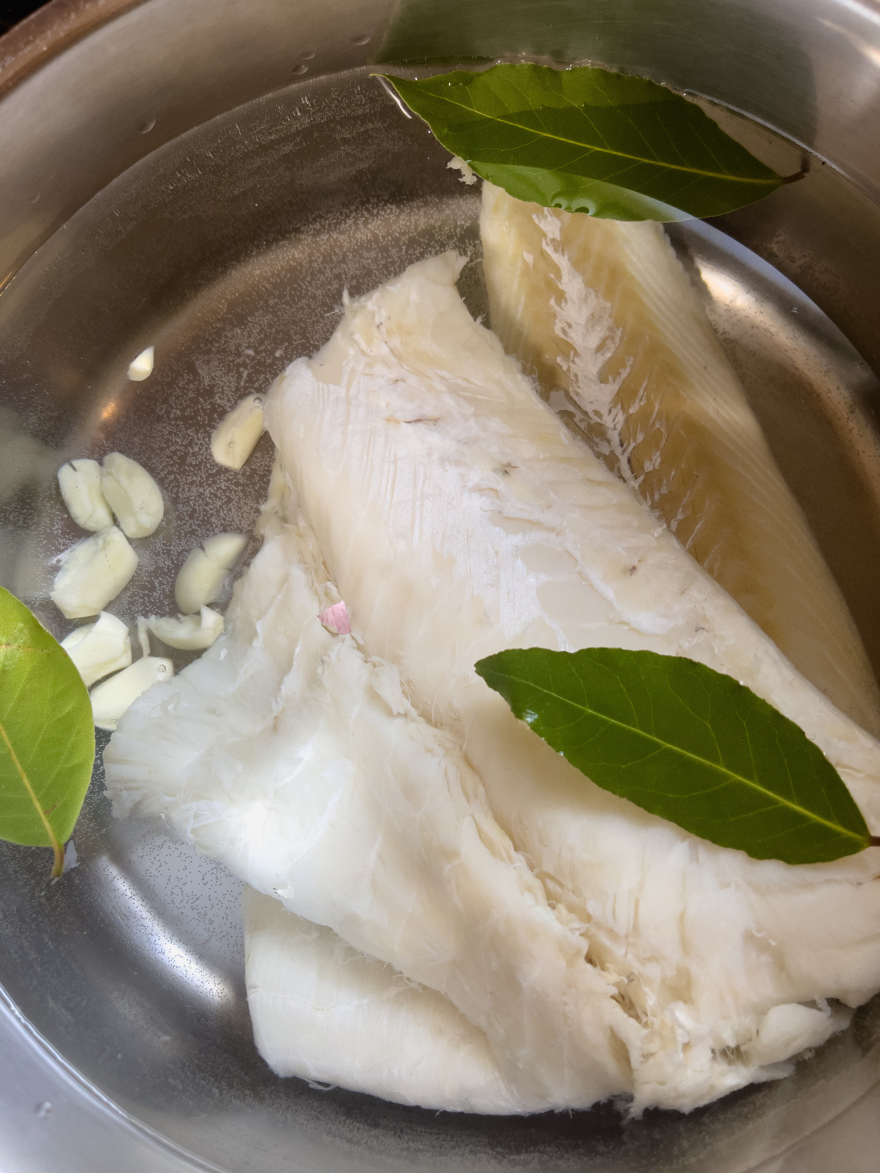 Salt cod, bay leaves and garlic in a pot with water, ready to start cooking.