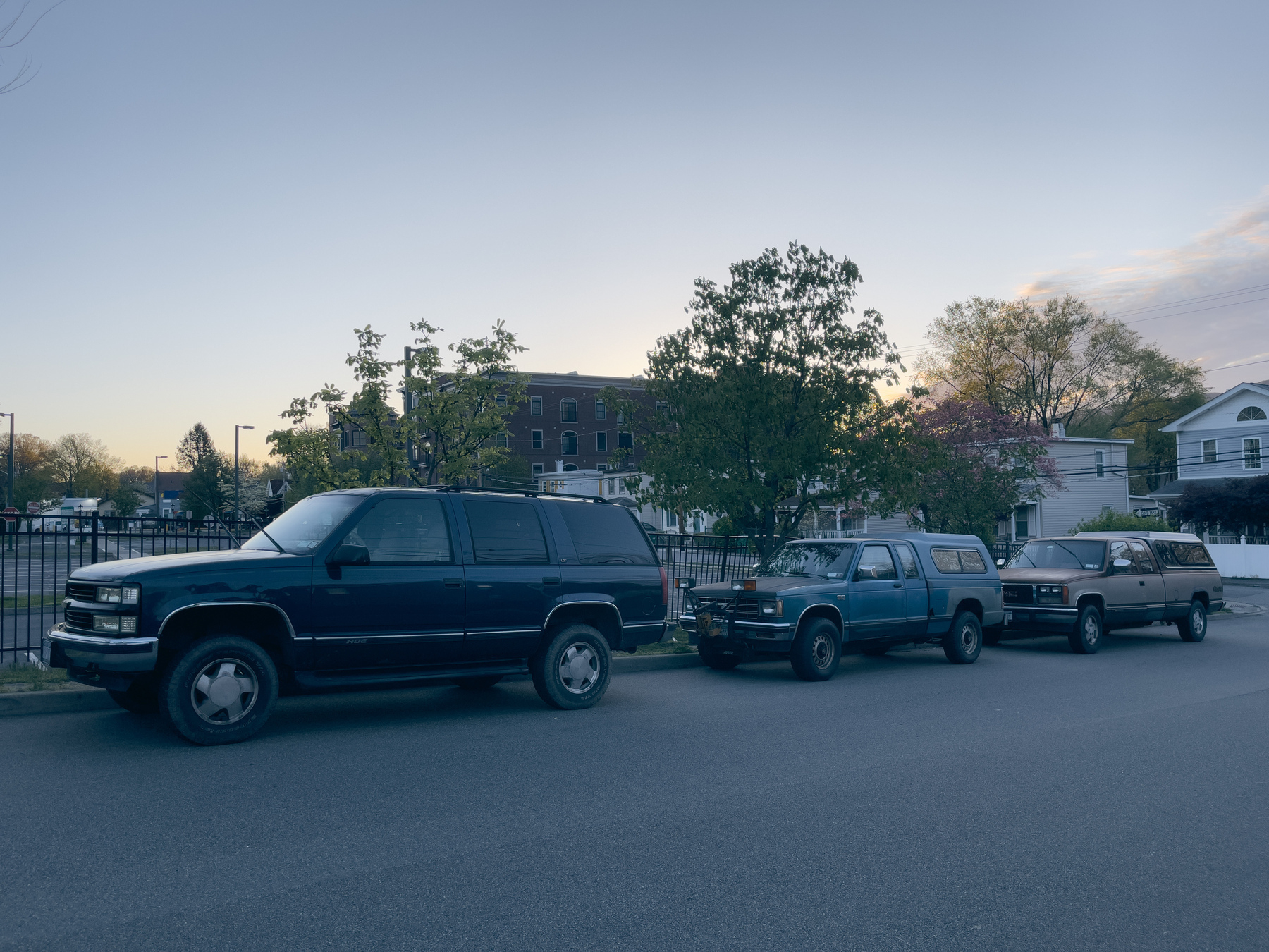 Three old pickup trucks in a row. Streetscape early morning.