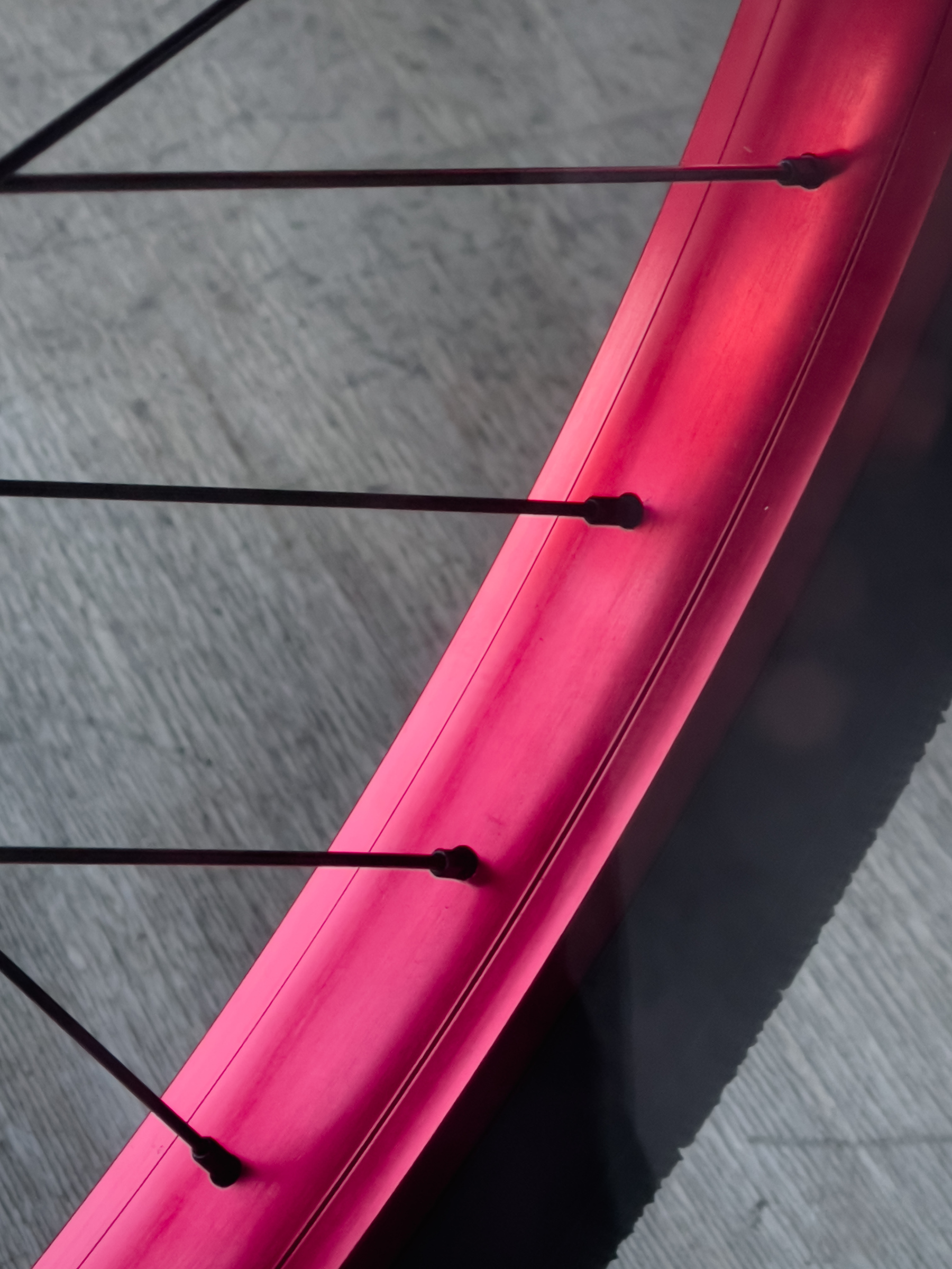 Closeup of bicycle tire rim curving from upper right to lower left. The rim is a beautiful hue of pink-red-orange.