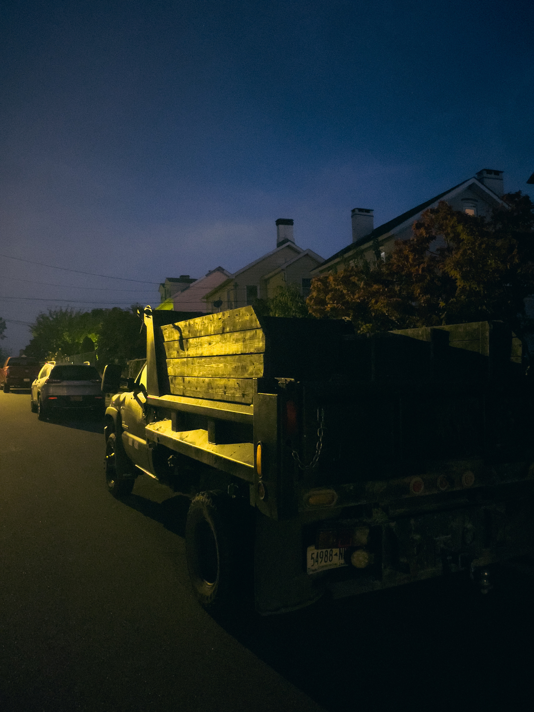 Small truck, and car illuminated by streetlights, early morning.