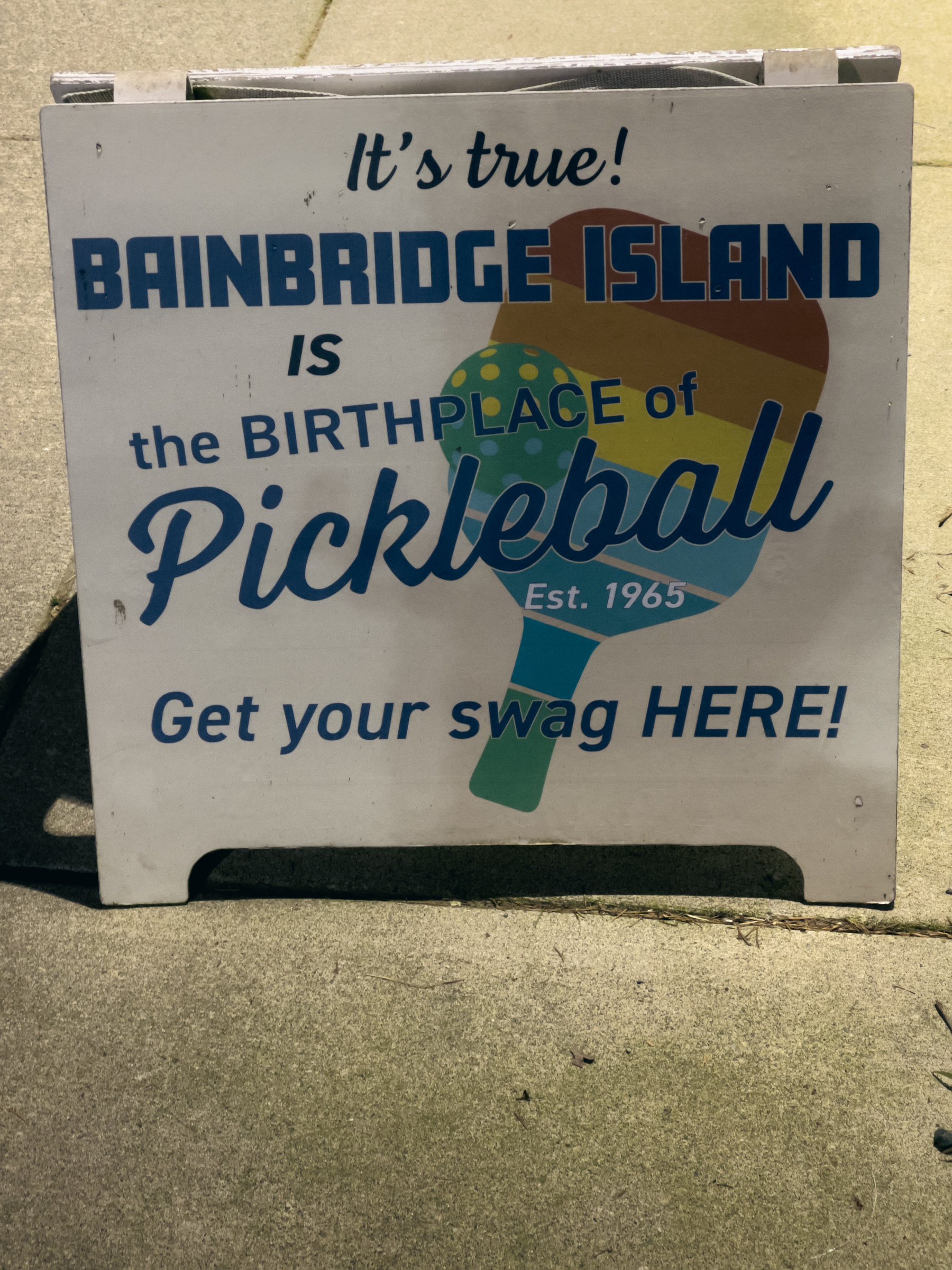 Sandwich sign with “It’s true! Bainbridge Island is the birthplace of Pickleball. Est 1965. Get your swag HERE!