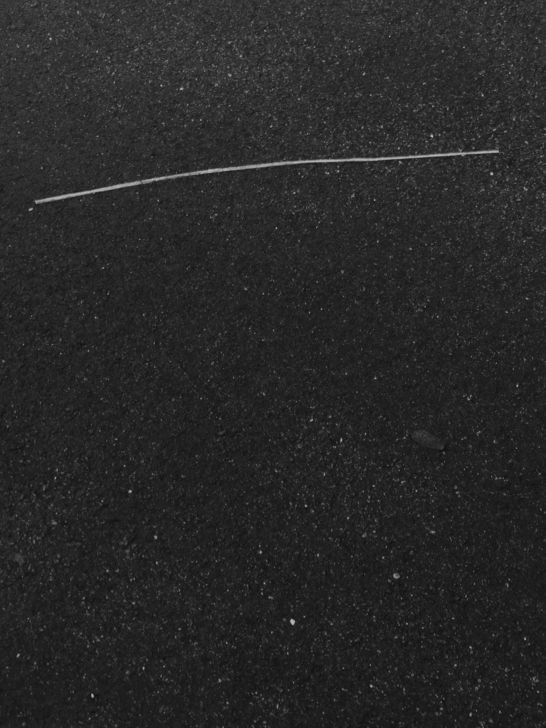 Abstract composition of gently curved strip of plastic running across top of vertically framed asphalt pavement section.