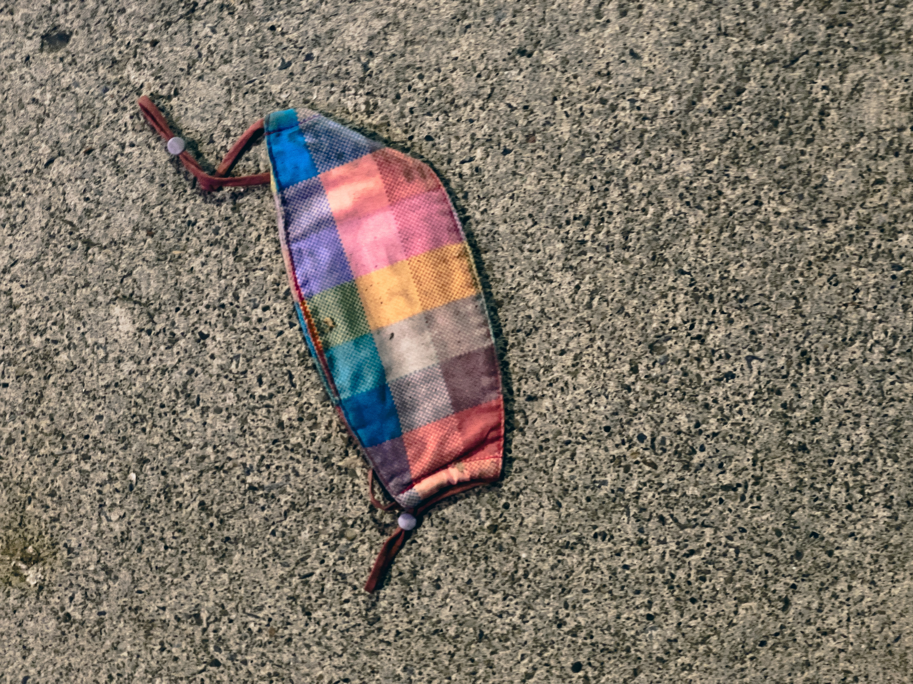Multicolored plaid cloth mask on concrete pavement.