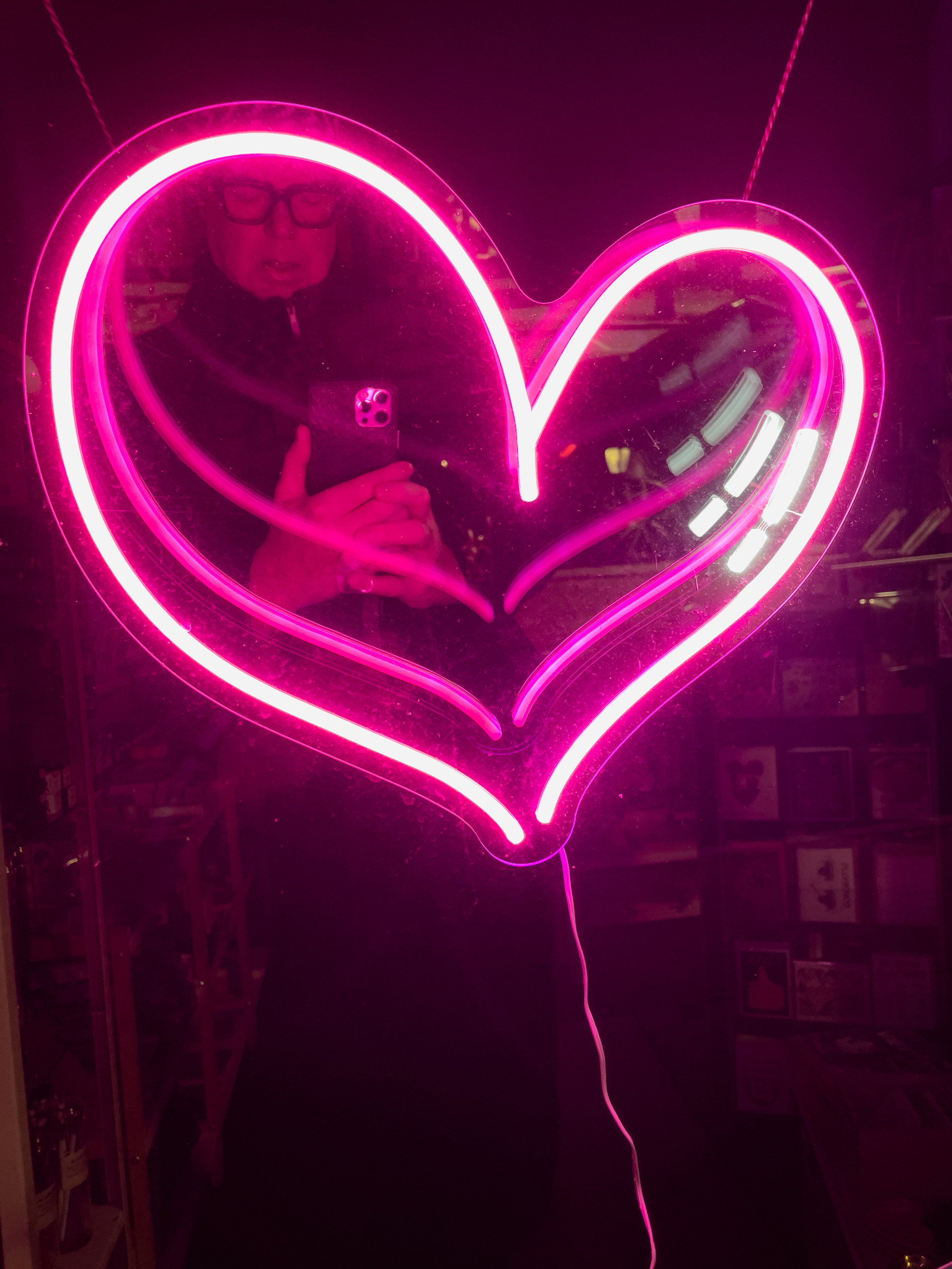 Selfie in the left lobe of a neon heart in a shop window.